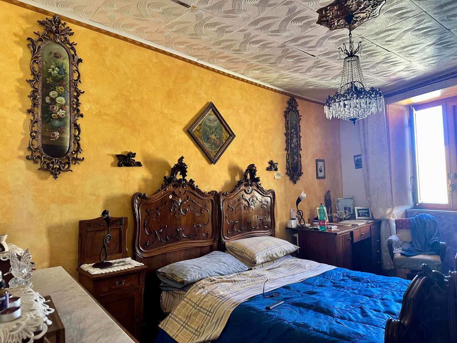 Antico soggiorno in stile classico con mobili in legno intagliato, decorazioni elaborate, chandelier e pareti gialle calde, ideale per spazi abitativi eleganti e tradizionali.