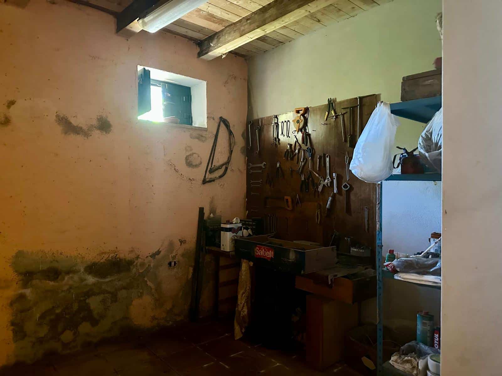 Selvagene strumenti da lavoro attaccati al muro in una stanza rustica con pareti in pietra e piccola finestra, ambiente di officina o ripostiglio.