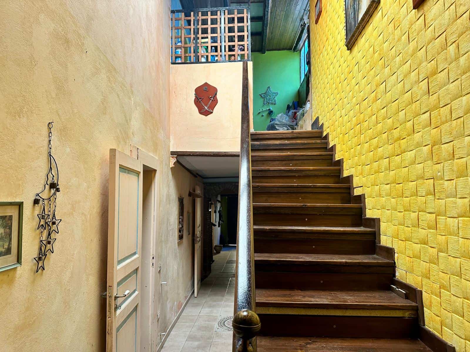 Scala in legno con ringhiera in ottone, ambiente interno con pareti colorate e decorazioni, stile rustico e accogliente.
