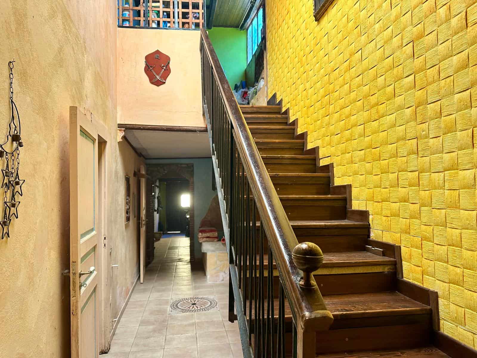 Scala in legno con ringhiera in ferro battuto, pareti colorate e decorazioni rustiche in stile tradizionale, ambientazione di una casa in stile rustico o tradizionale.