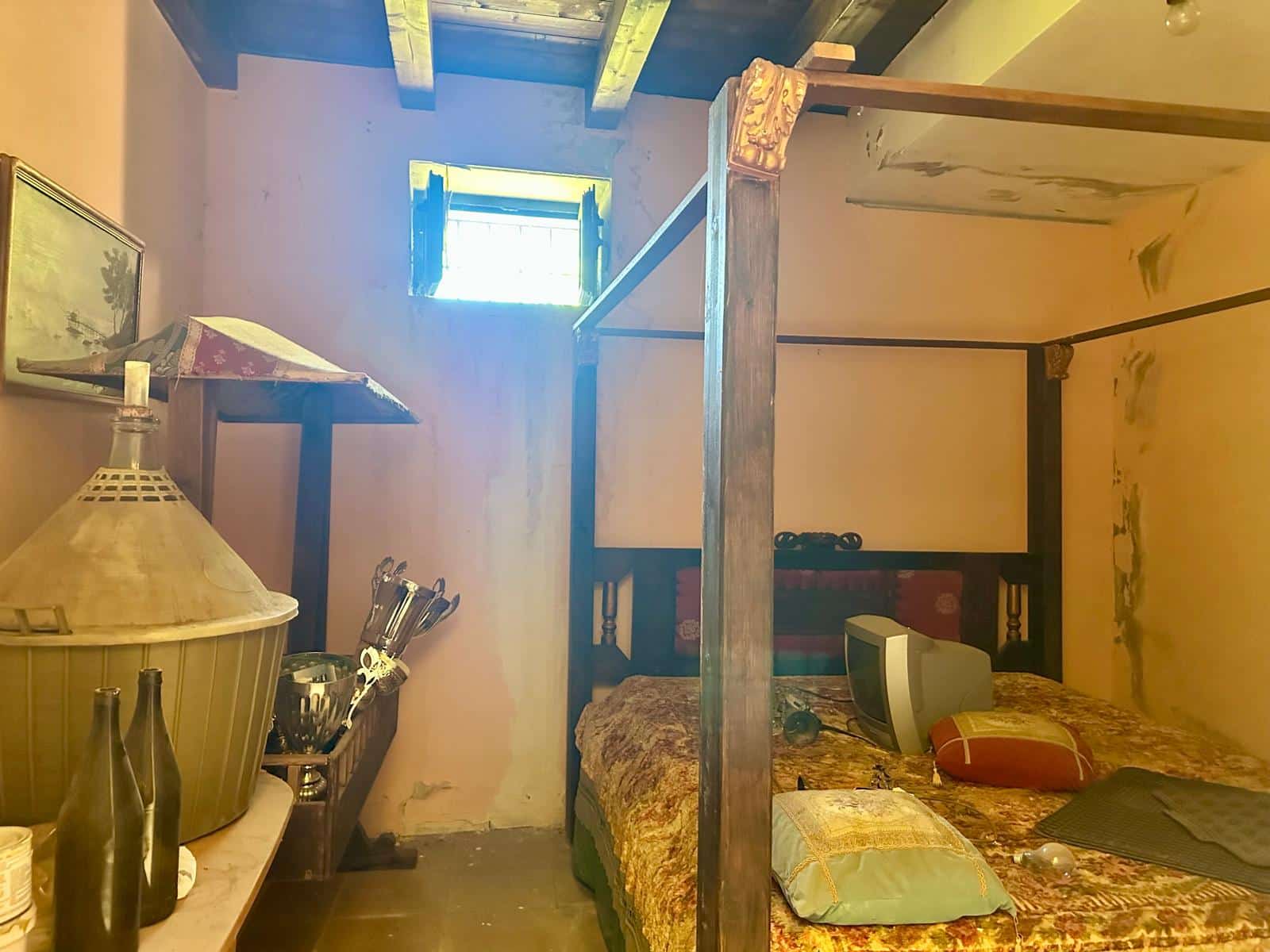 Foto di una camera da letto rustica con pareti colortte e un letto in legno antico, decorazioni vintage, finestra piccola con tende, atmosfera accogliente e autentica.