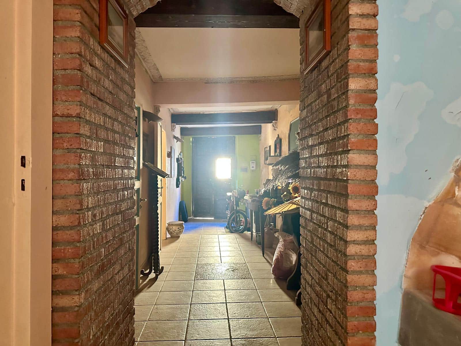 Scorcio dell'ingresso di casa con pareti in mattoni a vista e arredi rustici, stile tradizionale, dettagli accoglienti, illuminazione naturale, progetto di ristrutturazione casa, arredamento vintage, atmosfera calda e familiare.