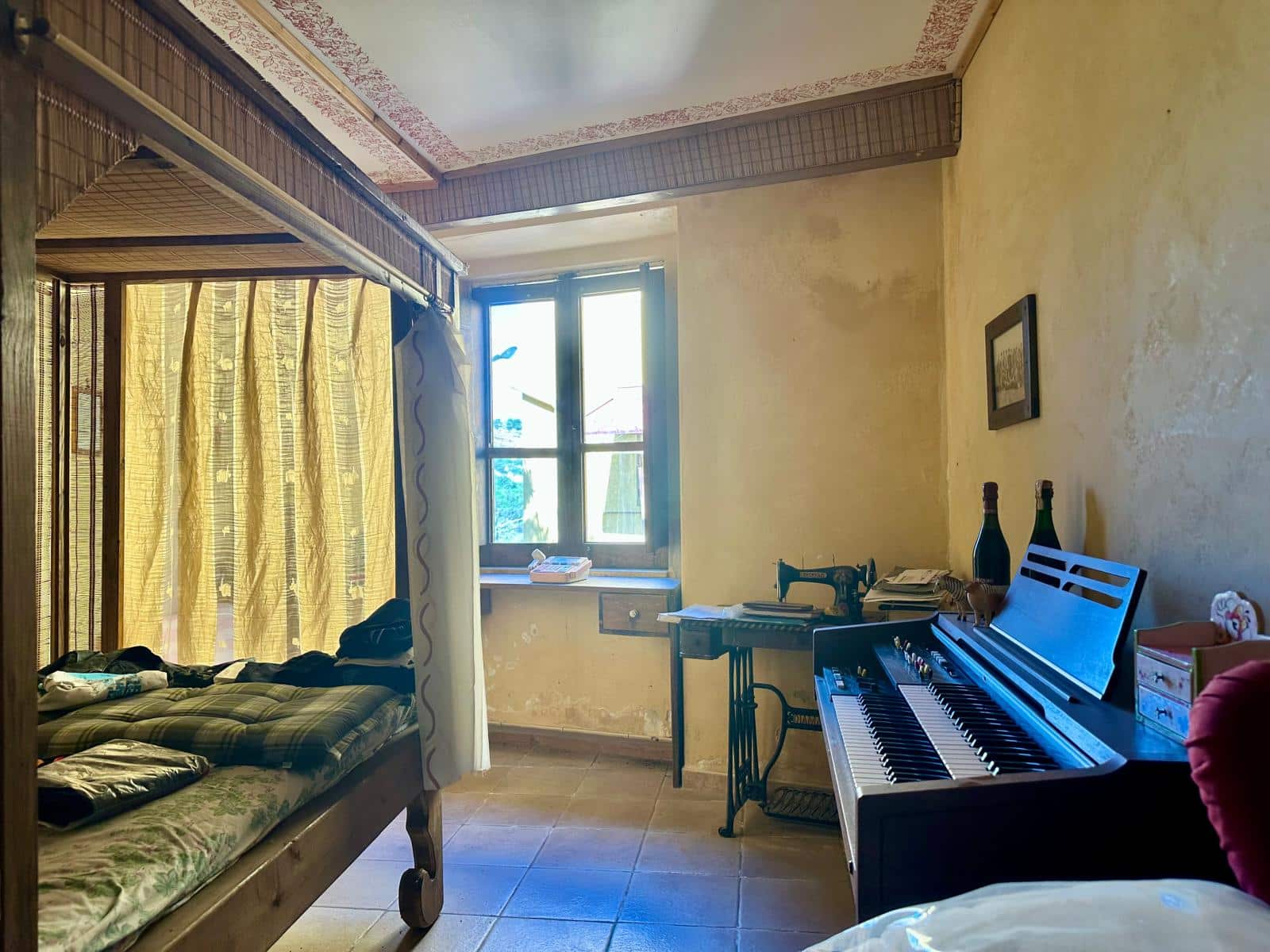 Letto a baldacchino in una stanza spaziosa con pareti gialle e soffitto decorato, finestra luminosa con tende gialle, console con oggetti vari, e un pianoforte nero con accessori musicali.