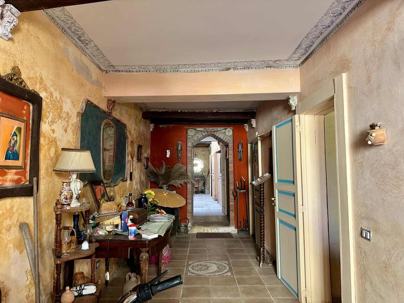 Valore alt: Ingresso di casa rustica con pareti dai colori caldi, decorazioni d'epoca, oggetti vintage e arredi eleganti, ambiente accogliente e ricco di stile.