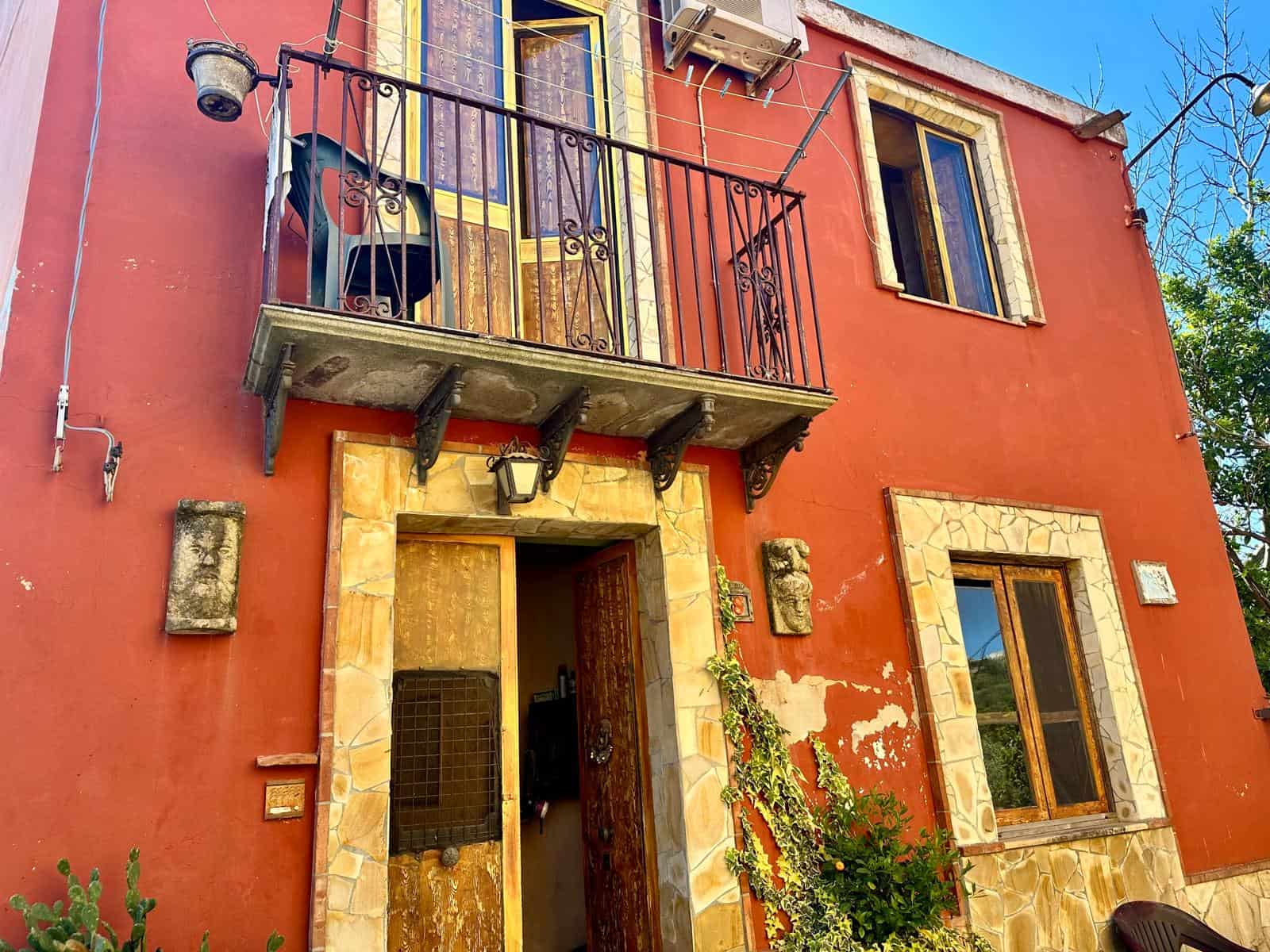 Rustico ristrutturato con balcone in ferro battuto, pareti rosse e dettagli in pietra, ideale per investimenti o residenza, immerso nel verde con caratteristiche di charme e autenticità.