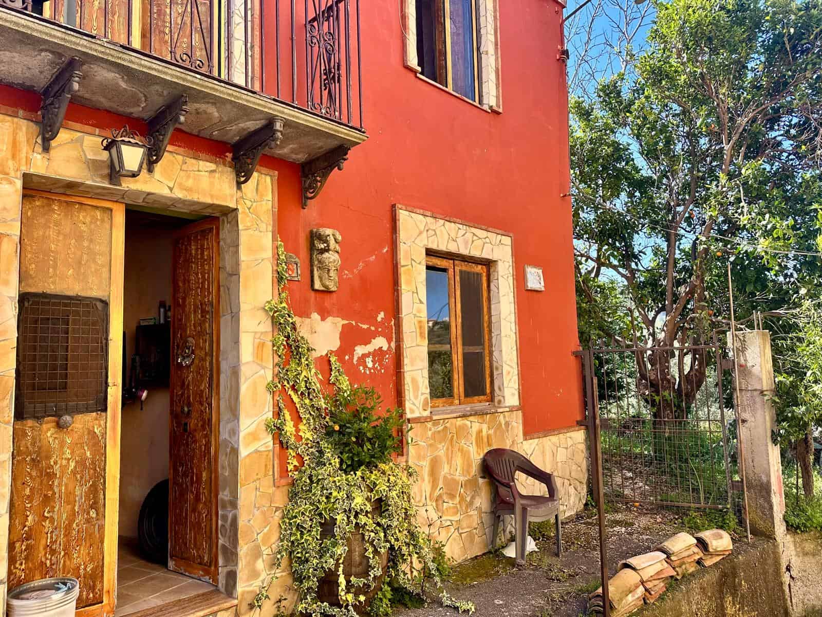 Casa in stile rustico con pareti color terracotta, dettagli in pietra e legno, giardino con piante verdi, ingresso accogliente e atmosfera calda e rustica, ideale per case di campagna o vacanze in campagna.