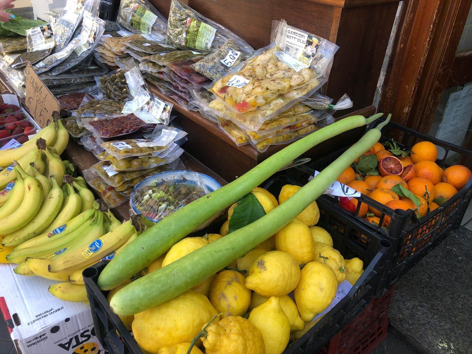 Fiorettini di zucchina fresca con arance e banane di provenienza locale, vendita di prodotti ortofrutticoli freschi e di qualità.