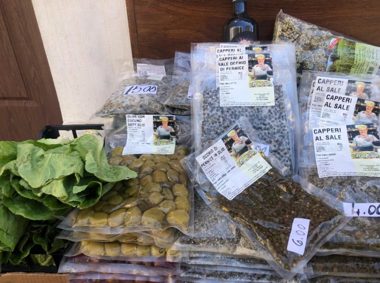 Olive sott'olio e capperi freschi in confezioni sigillate, alimenti tipici della cucina mediterranea, disponibili presso il mercato locale di NextCasa.