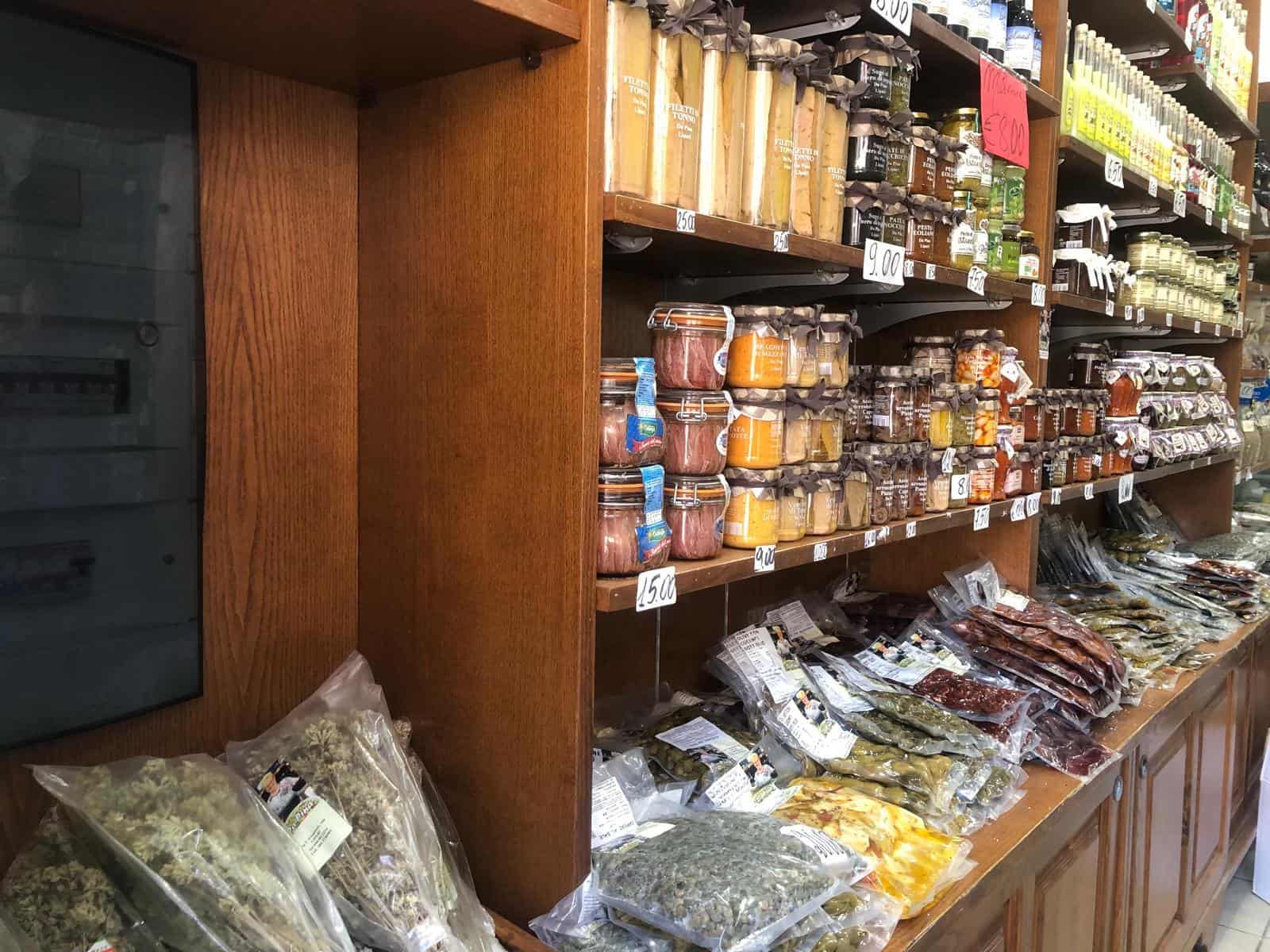 Fianco di scaffale di alimenti in negozio di alimentari con conserve, spezie e prodotti sottovuoto, esposizione di prodotti biologici e alimentari di alta qualità per cucinare ricette italiane autentiche.