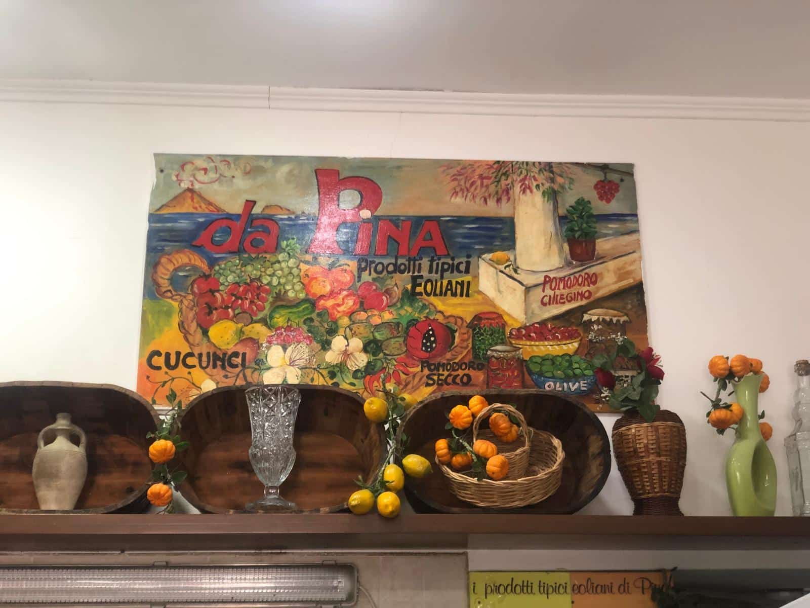 Vassoio di legno con decorazioni di agrumi e bottiglie di ceramica, in un ambiente con quadri colorati a tema prodotti tipici italiani, rappresentando un mercato di frutta e verdura.