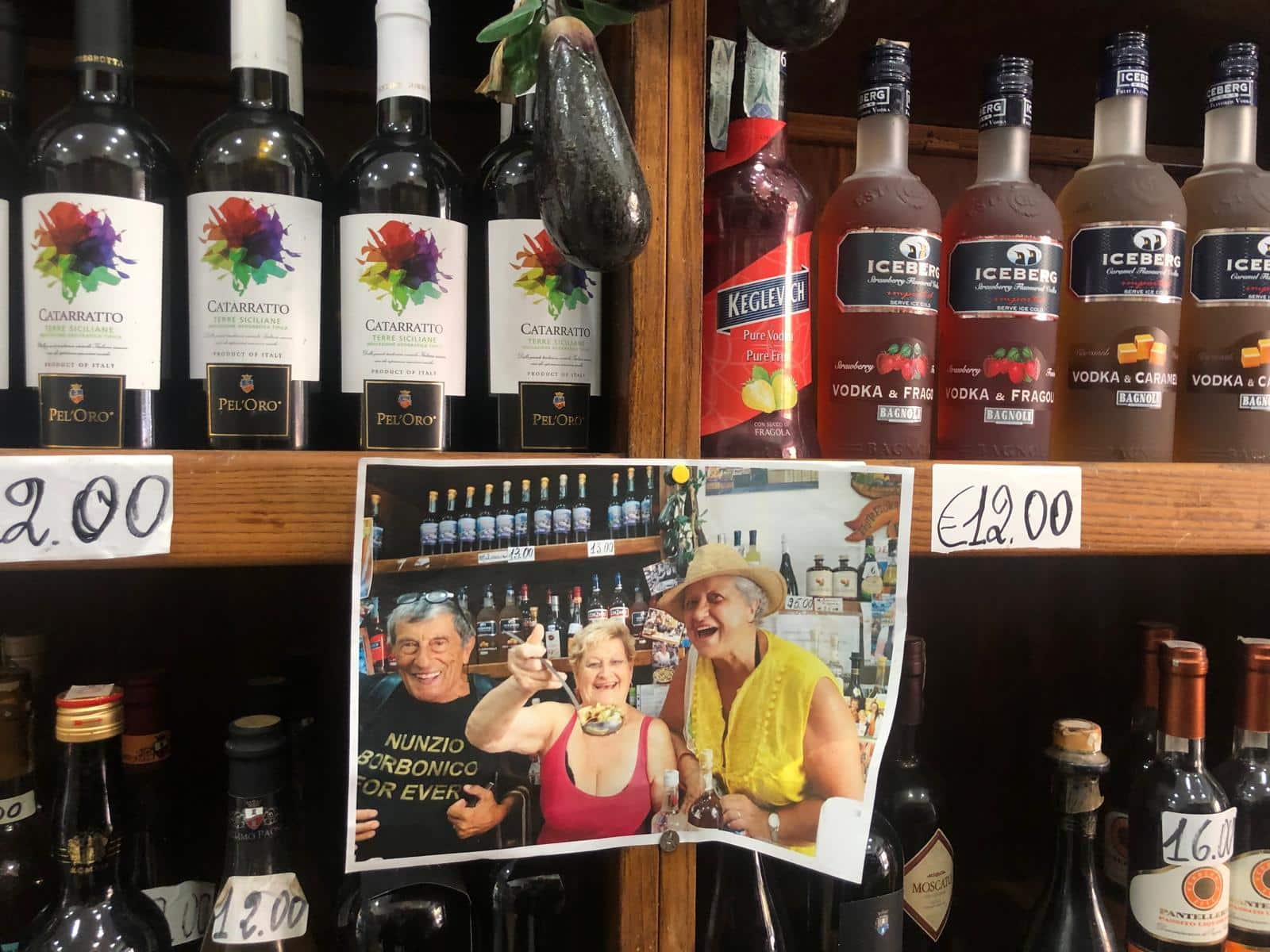 Bottiglie di liquori e vini sull'esposizione in un negozio con una foto di clienti che si divertono al bancone.