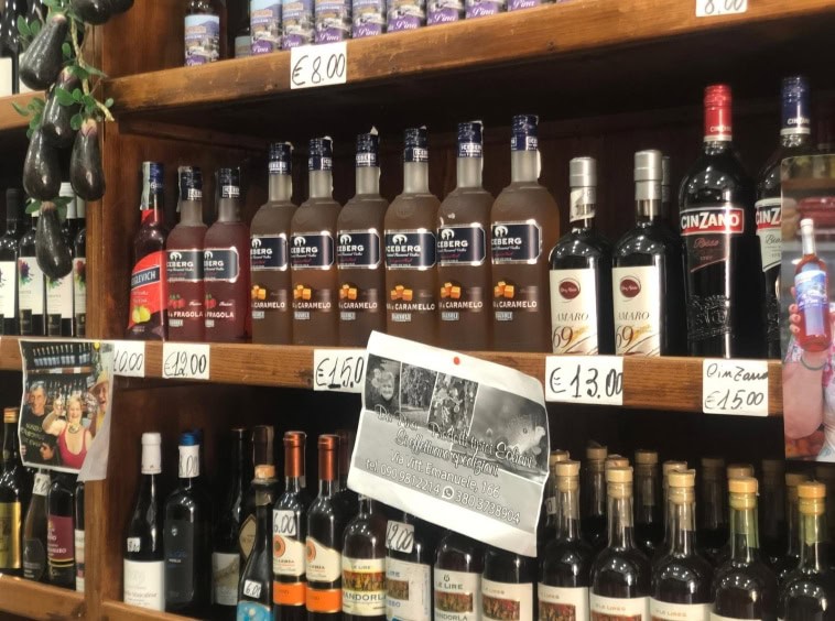 Bottiglie di liquori e alcolici sugli scaffali di un negozio alimentare italiano, con prezzi evidenziati e volantini pubblicitari, in un ambiente che evidenzia prodotti di qualità e tradizione.