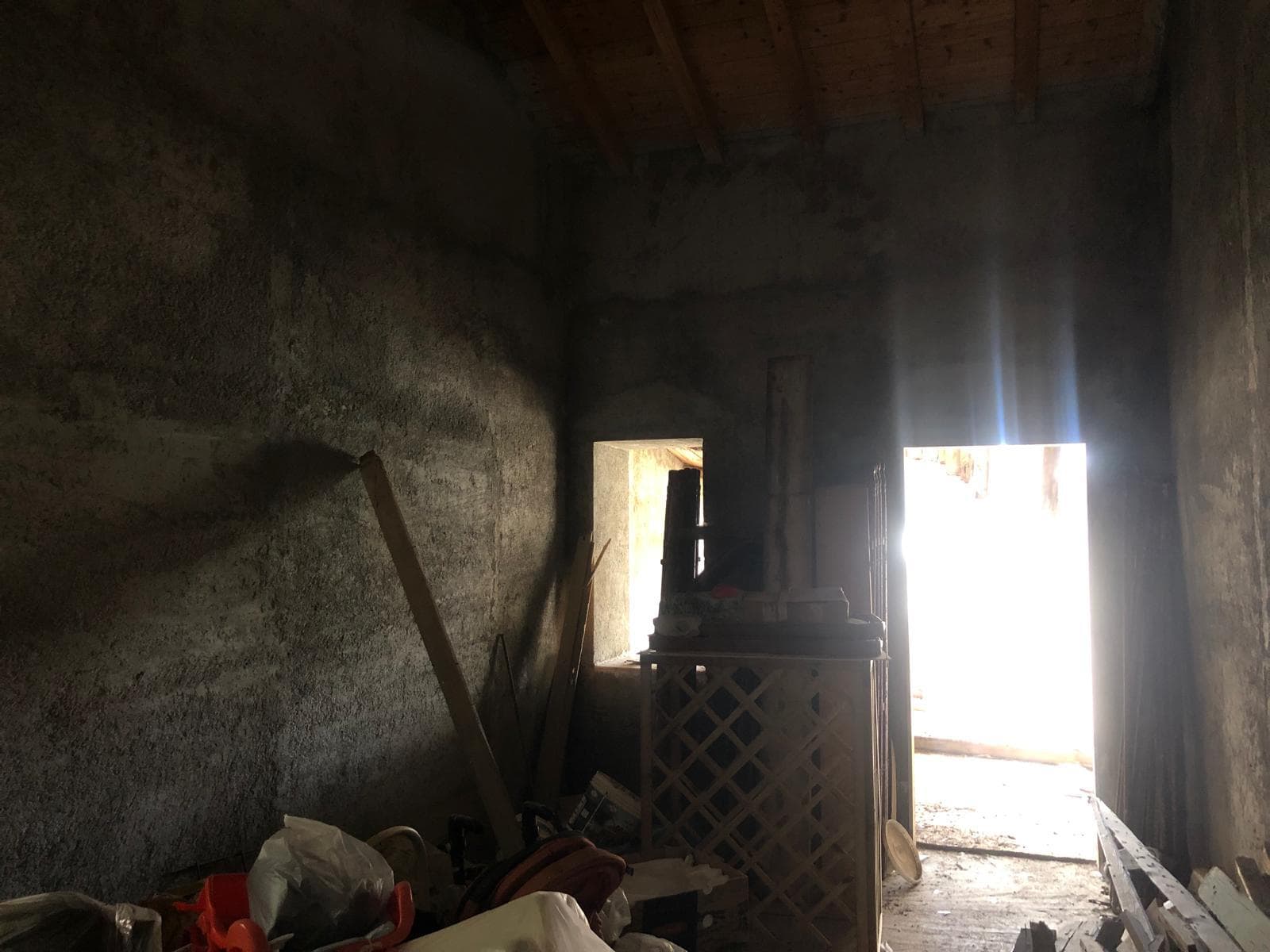 Interno rudimentale di una casa in fase di ristrutturazione, con pareti in pietra e apertura verso la luce esterna, spazioso e rustico, ideale per interventi di restauro e miglioramento abitativo.