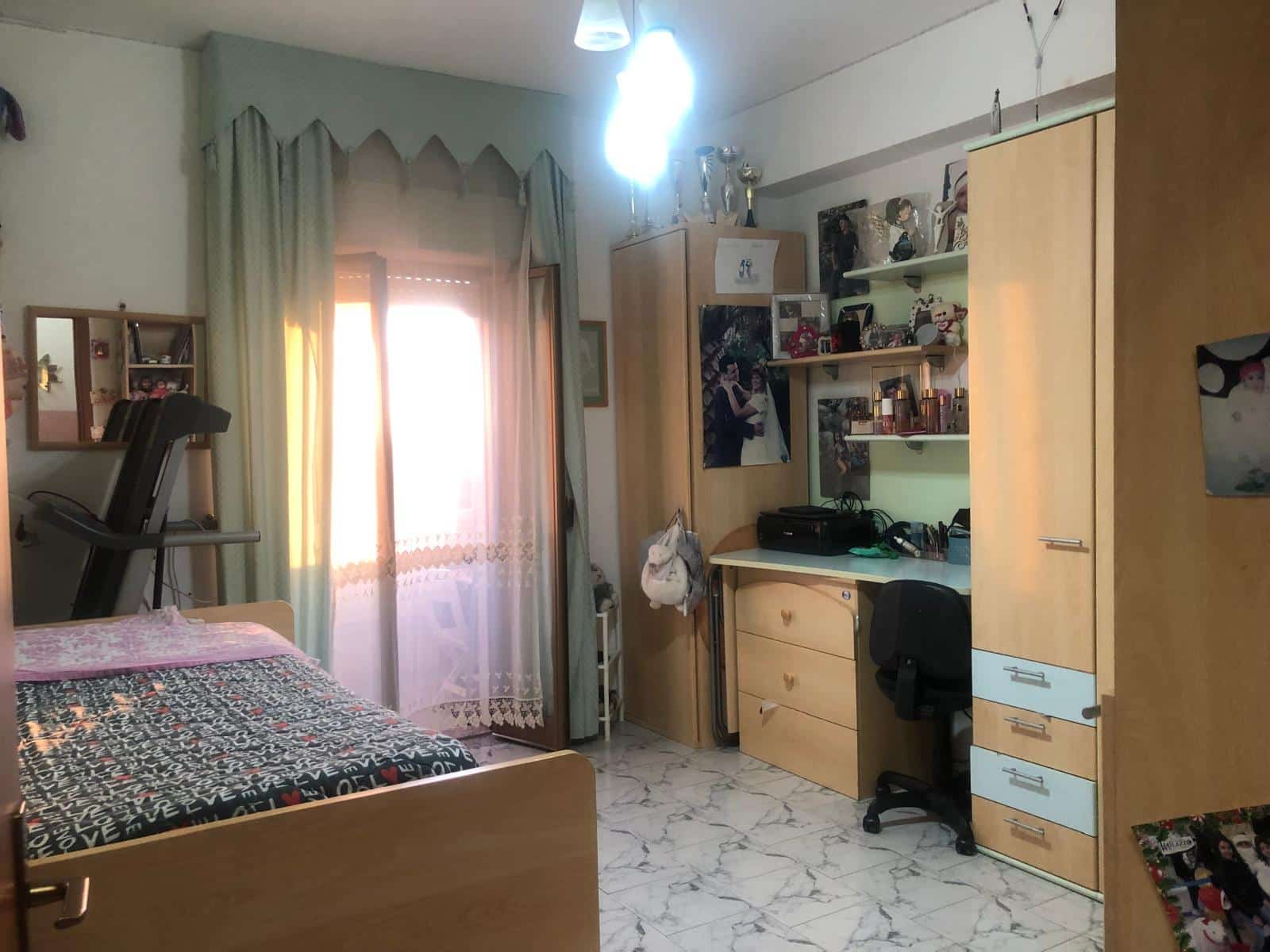 Armadio e scrivania con decorazioni, camera da letto con letto e porta finestra con tende, ambienti studi e relax, arredamento funzionale, spazio personale ben organizzato, NextCasa.