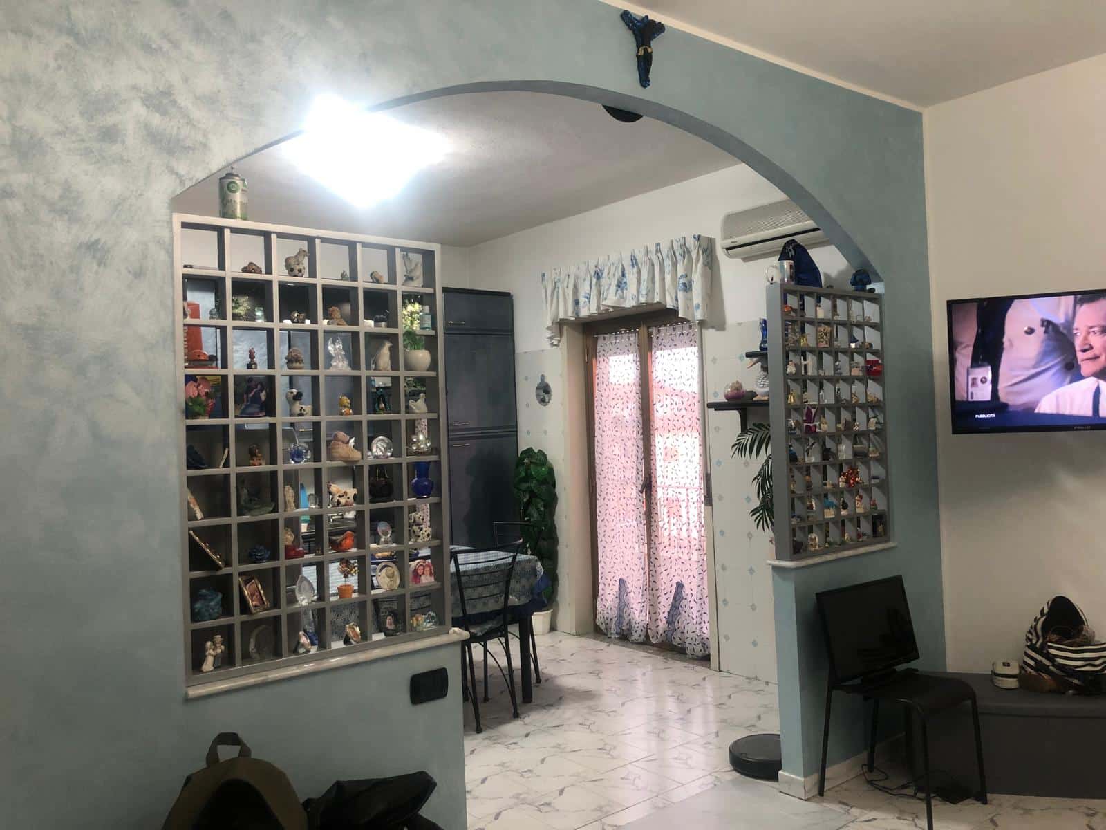 Vetrina con decorazioni e souvenir in casa moderna, salotto con mobile diviso e TV, ambiente accogliente e ben illuminato, ideale per investimenti immobiliari o acquisti di proprietà Residenziali.
