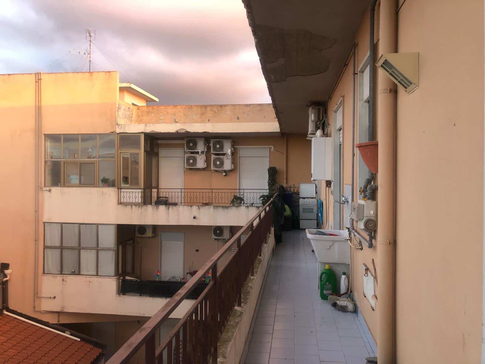 Balcone di un appartamento con elettrodomestici, piante e riscaldatori, vista su altri edifici con balconi e aria condizionata, all'aperto, atmosfera urbana, progetto NextCasa.