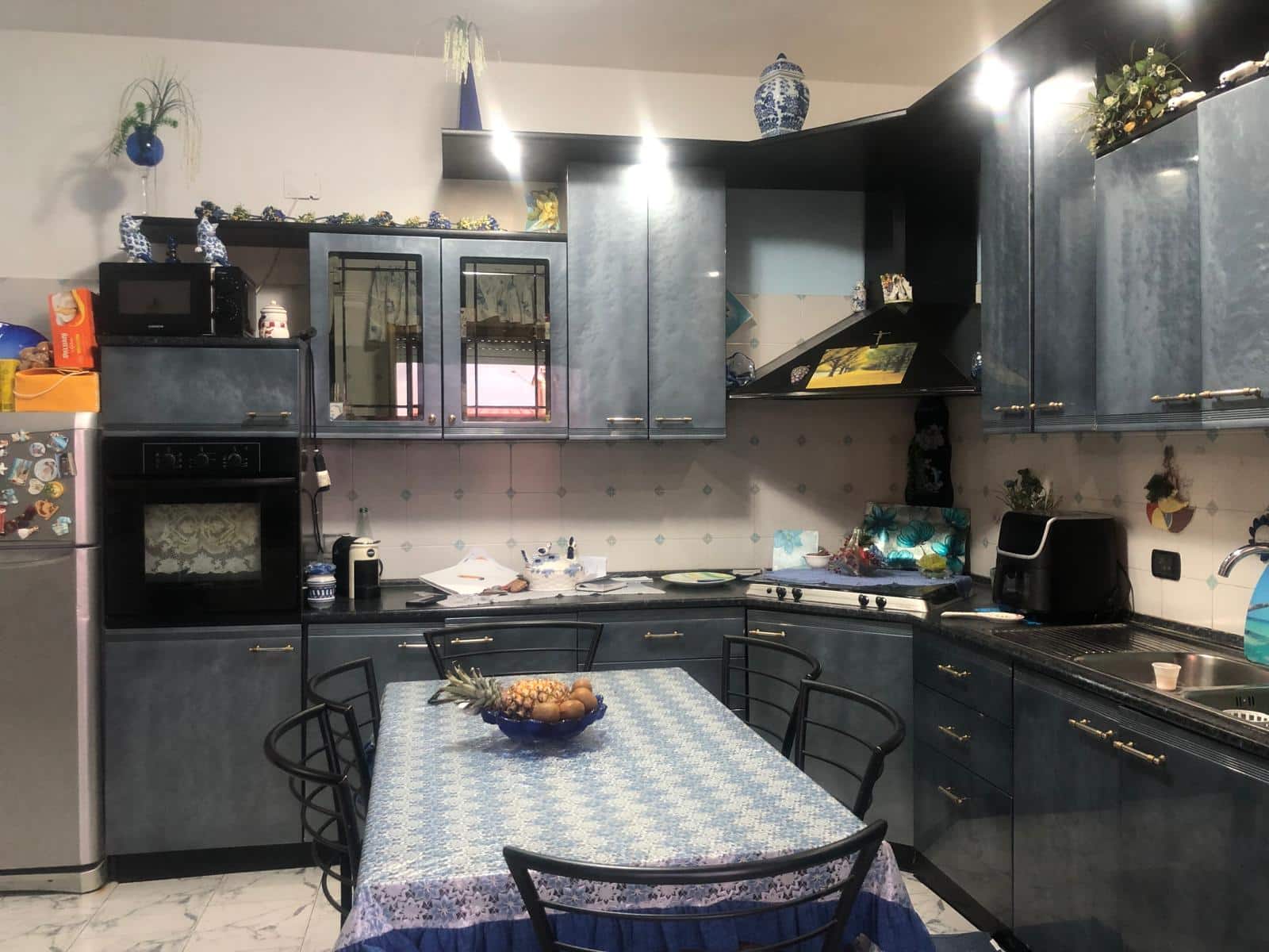 Cucina spaziosa con mobili blu, elettrodomestici, tavolo ricoperto da tovaglia e decorazioni floreali, ideale per vivere momenti di convivialità e cucina casalinga.