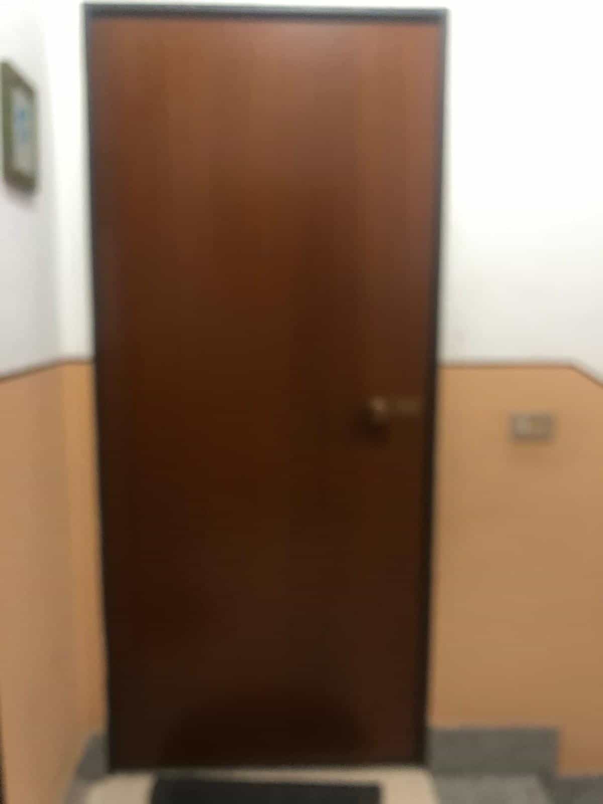 Porta in legno scuro, ingresso di un appartamento con pareti beige e dettagli arancioni, interruttore e quadro elettrico laterali, ambiente interno.