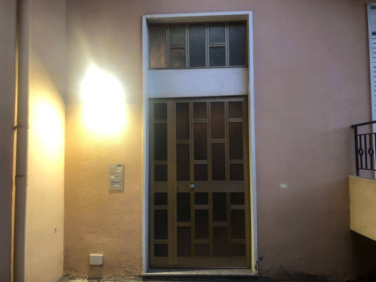 Porta d'ingresso in legno con vetri colorati e modulo blindato, situata in un edificio residenziale con pareti di colore beige e illuminazione esterna.