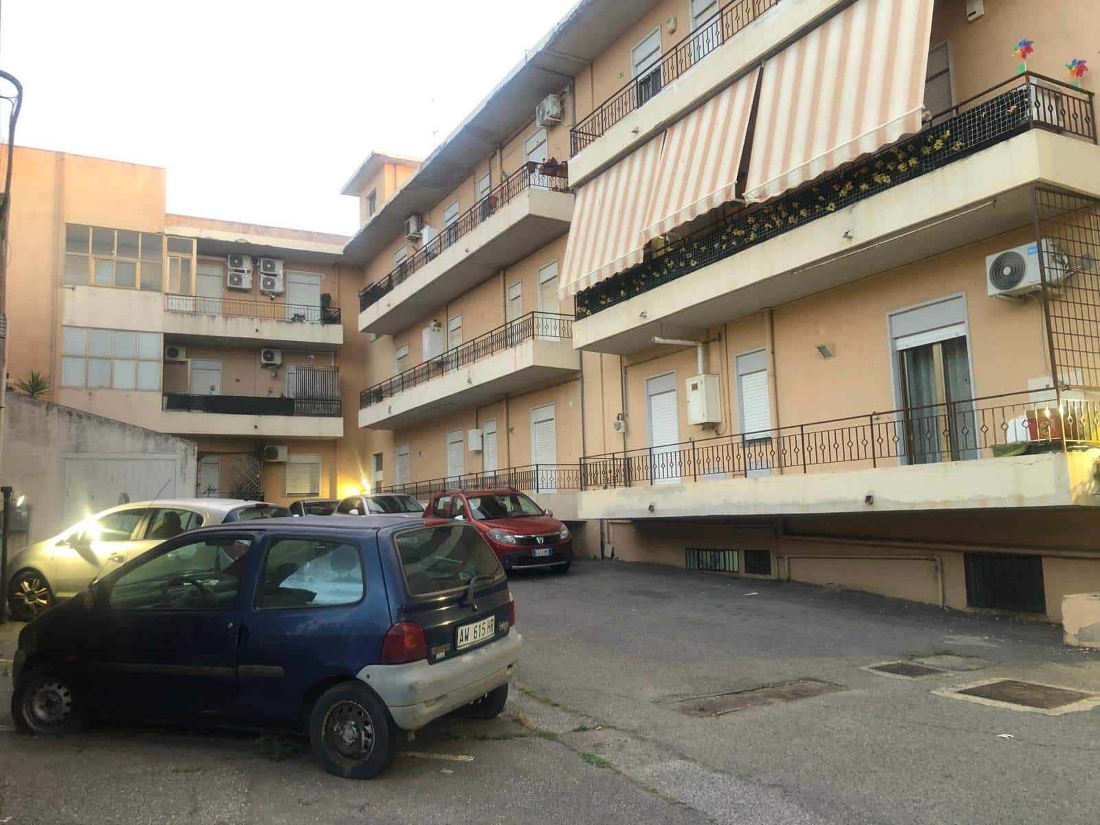 Auto parcheggiate davanti a un edificio residenziale con appartamenti, balconi e aria condizionata, in un contesto urbano, rappresentando soluzioni di alloggio e affitti immobiliari a NextCasa.