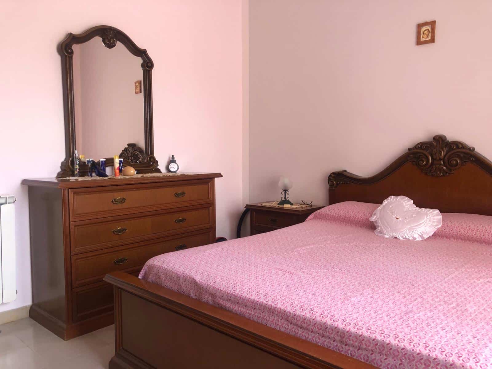 Arredo camera da letto con letto matrimoniale in stile classico, mobili in legno scuro e dettagli decorativi eleganti, ambiente accogliente e ben arredato.