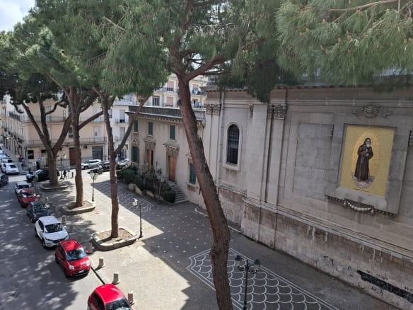 Auto in piazza con alberi e chiesa storica sullo sfondo, veduta urbana, architettura storica, parcheggio cittadino, ambiente urbano tradizionale, fotografia di strada, vista su strada con auto e edifici.