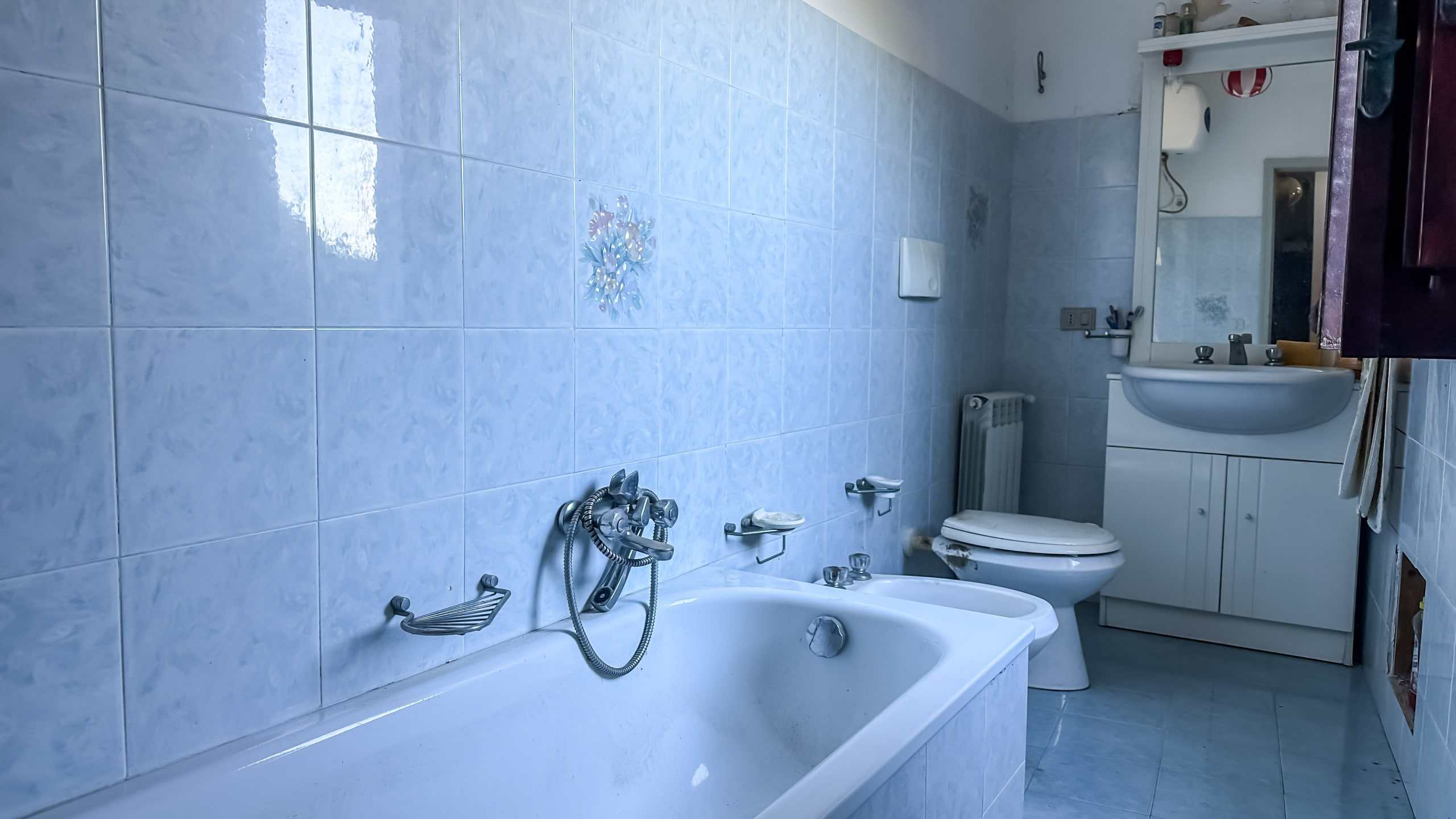Bagno moderno con vasca, WC e lavabo in stile classico, pareti rivestite con piastrelle azzurre e dettagli decorativi, spazio funzionale e luminoso, ideale per soluzioni abitative di qualità.