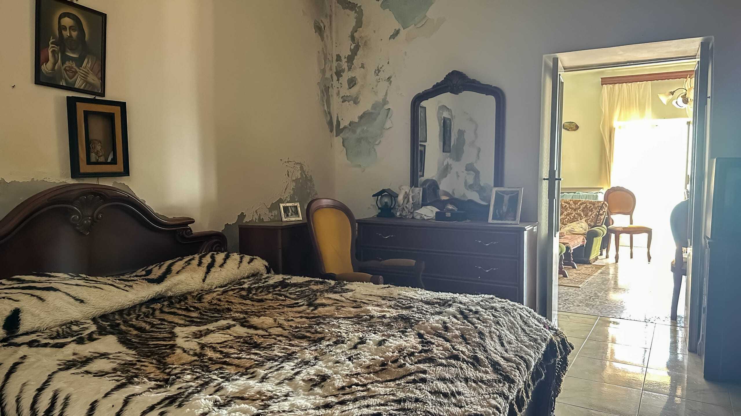 Vecchio letto in stile classico con copriletto animalier, mobili vintage, pareti con vernice scrostata, aria rétro e charm italiano, ambiente accogliente e unico, ideale per video e foto d’arredamento.