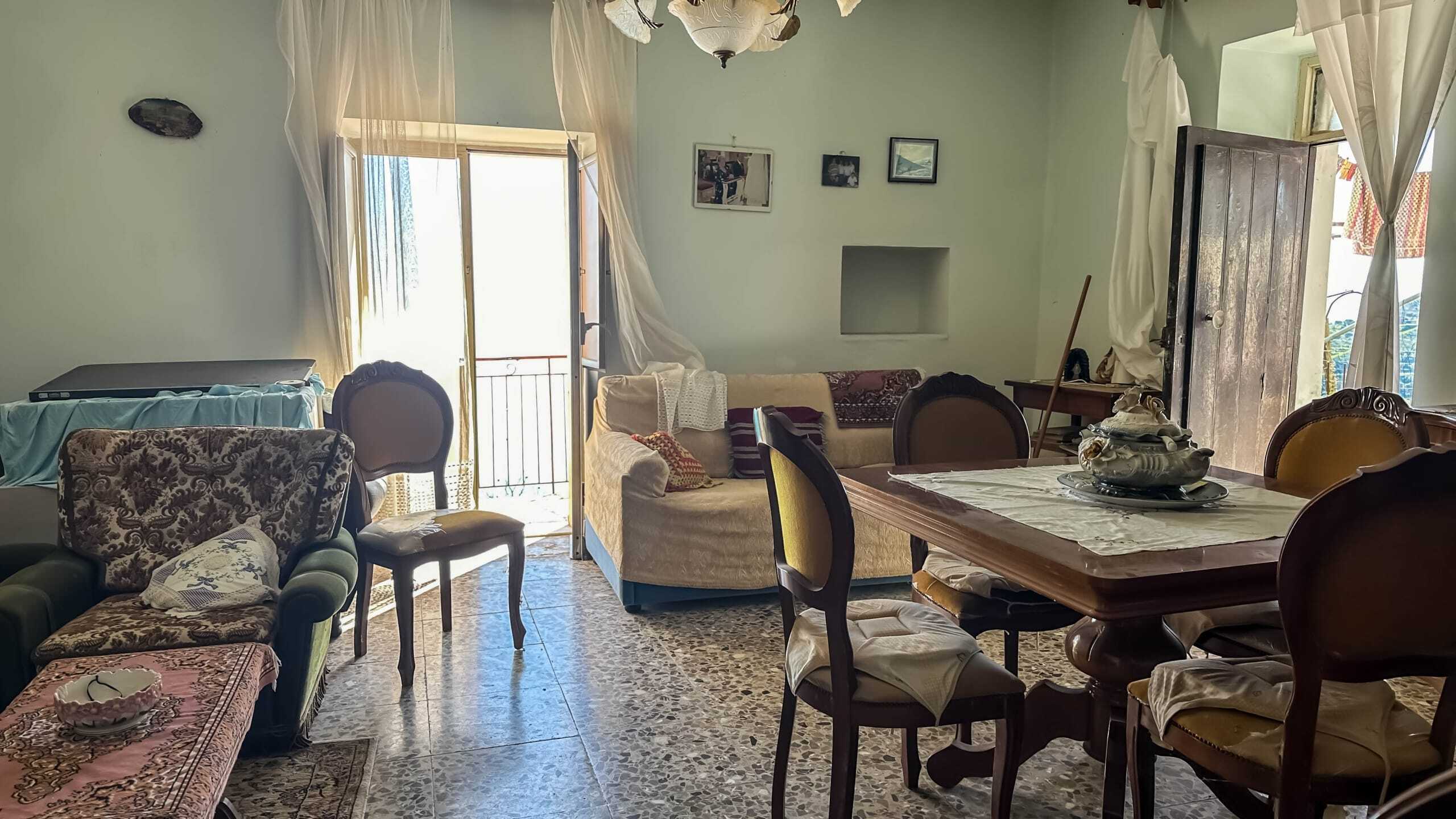 Soggiorno con divani e tavolo in legno, pareti chiare, porte con accesso al balcone, atmosfera familiare e accogliente, ideale per case vacanze e immobili residenziali.