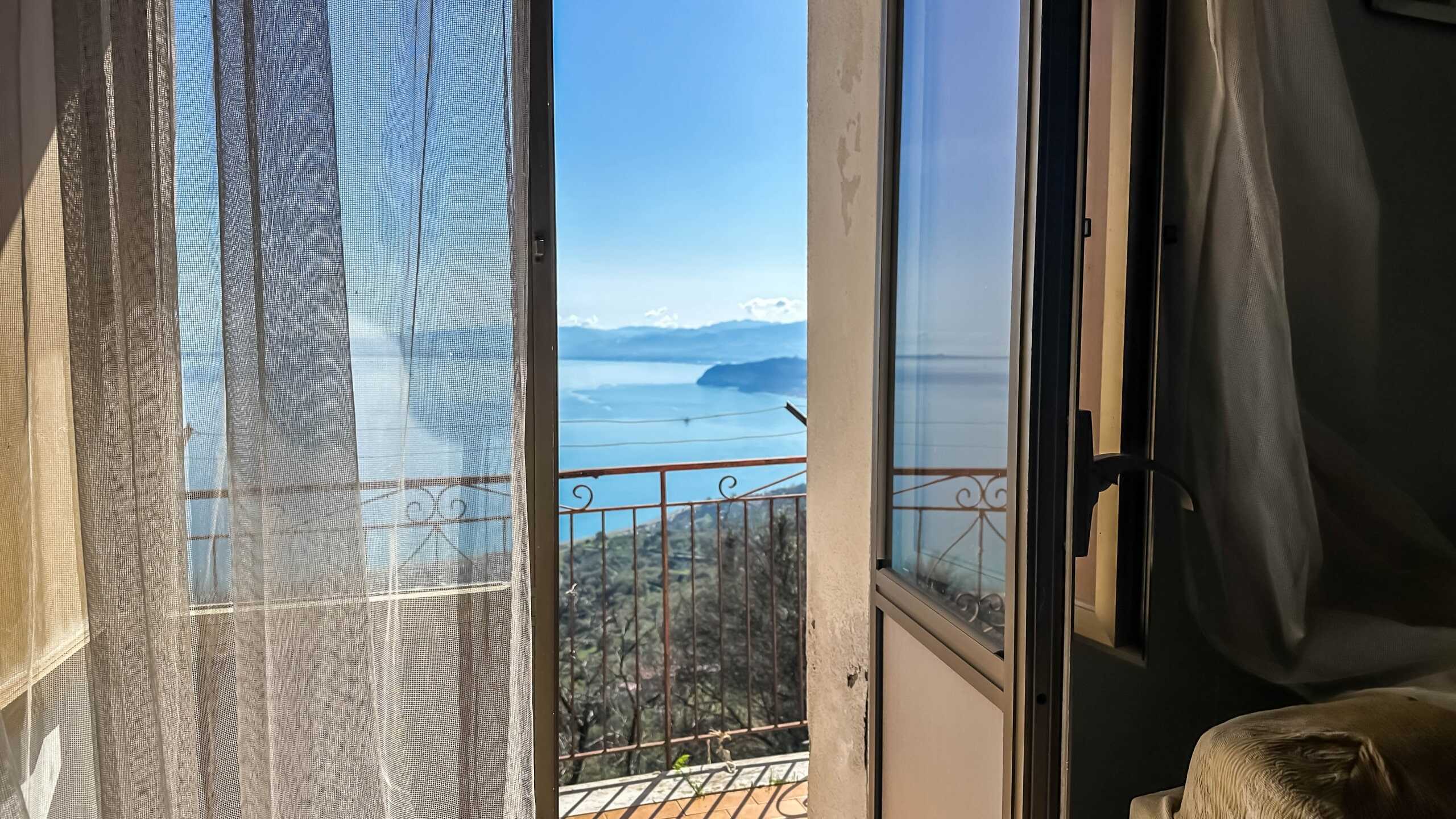 Vista mare e montagna dal balcone di un appartamento con balcone con ringhiera in ferro battuto, viaggio tra natura e comfort, immobile in vendita o affitto a NextCasa.