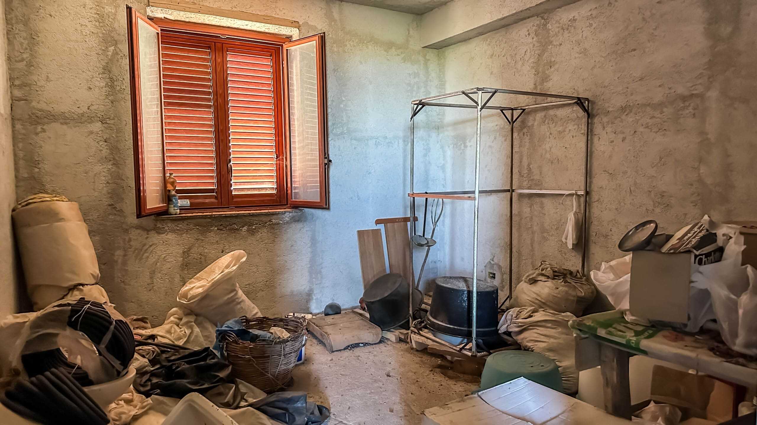 Vecchia soffitta non ristrutturata con finestra in legno, oggetti di bricolage, scatole e sacchi di utensili, in condizioni disordinate, ambiente rustico.