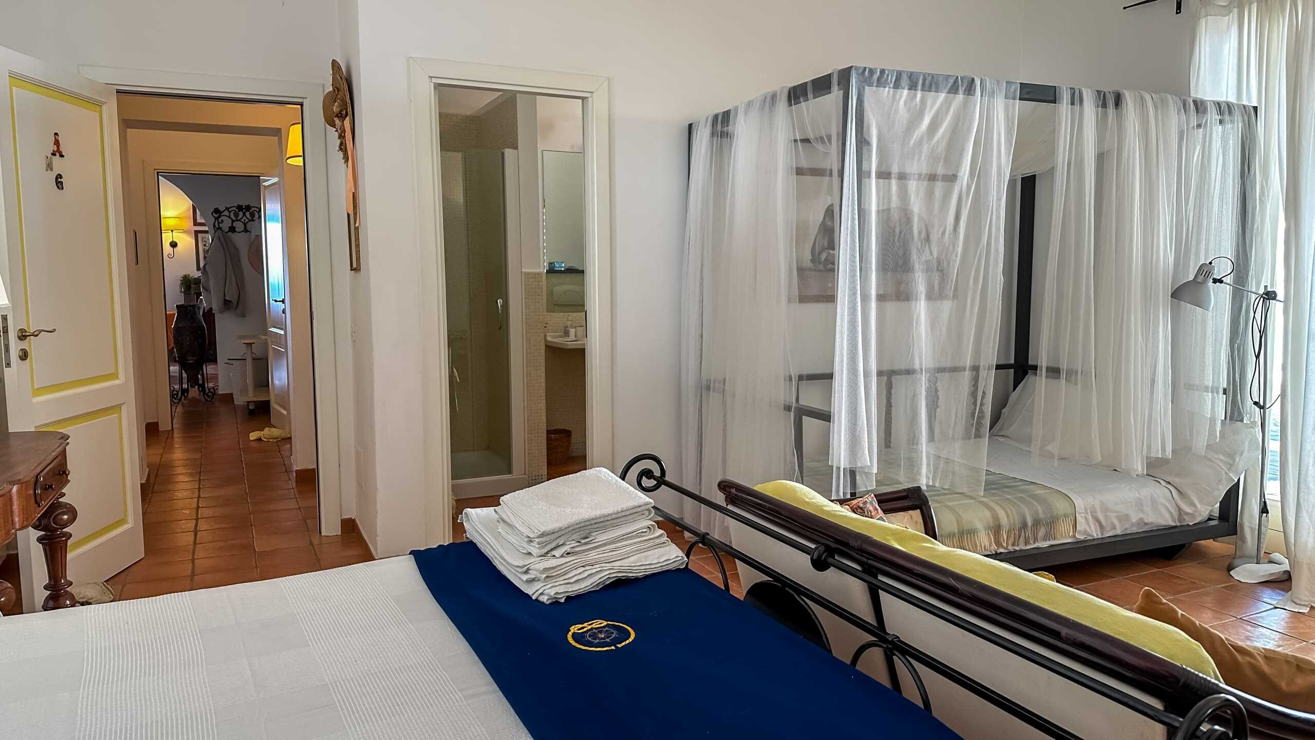 Letto matrimoniale con lenzuola bianche, ambientazione accogliente in stile casa vacanza NextCasa, camera con zanzariera e letto singolo, arredi eleganti, ideale per soggiorni relax in località turistica in Italia.