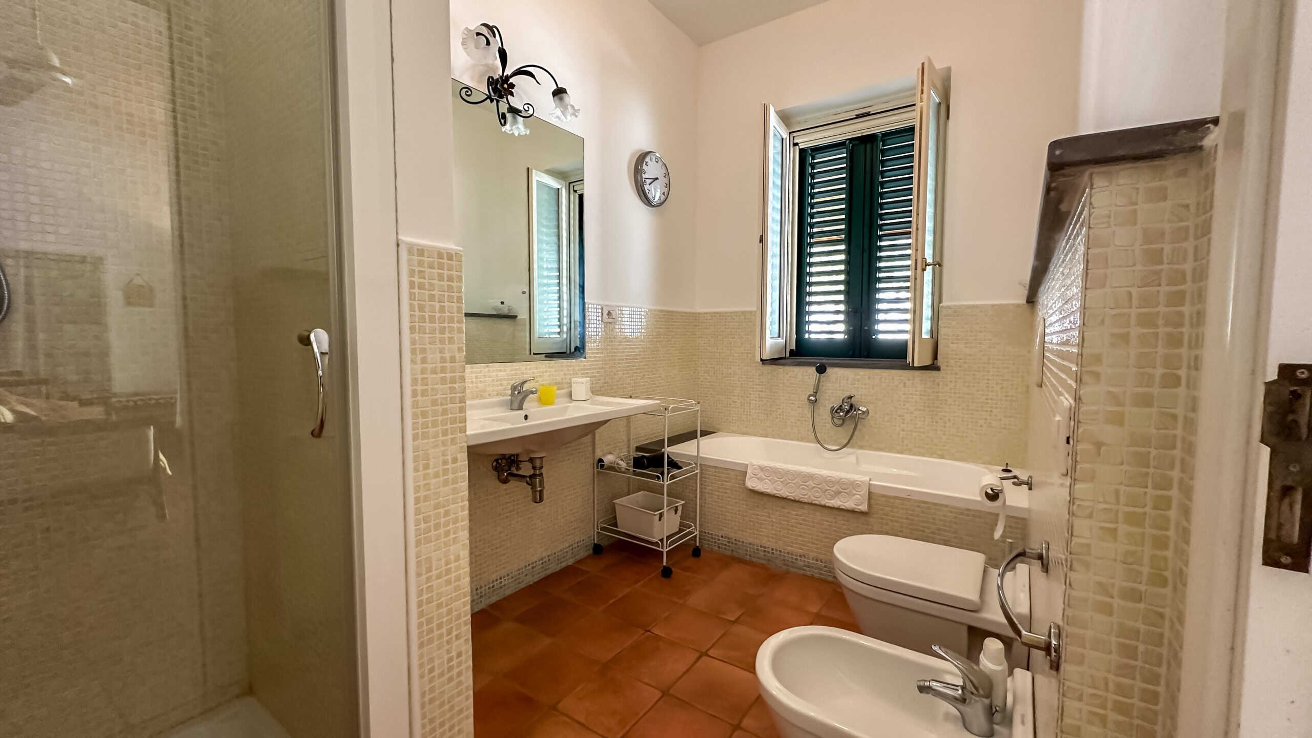 Bagno spazioso con vasca, bidet e lavabo, finestre con persiane in doppio stile, piastrelle beige, ambiente luminoso, arredi moderni, soluzione ideale per comfort e funzionalità.