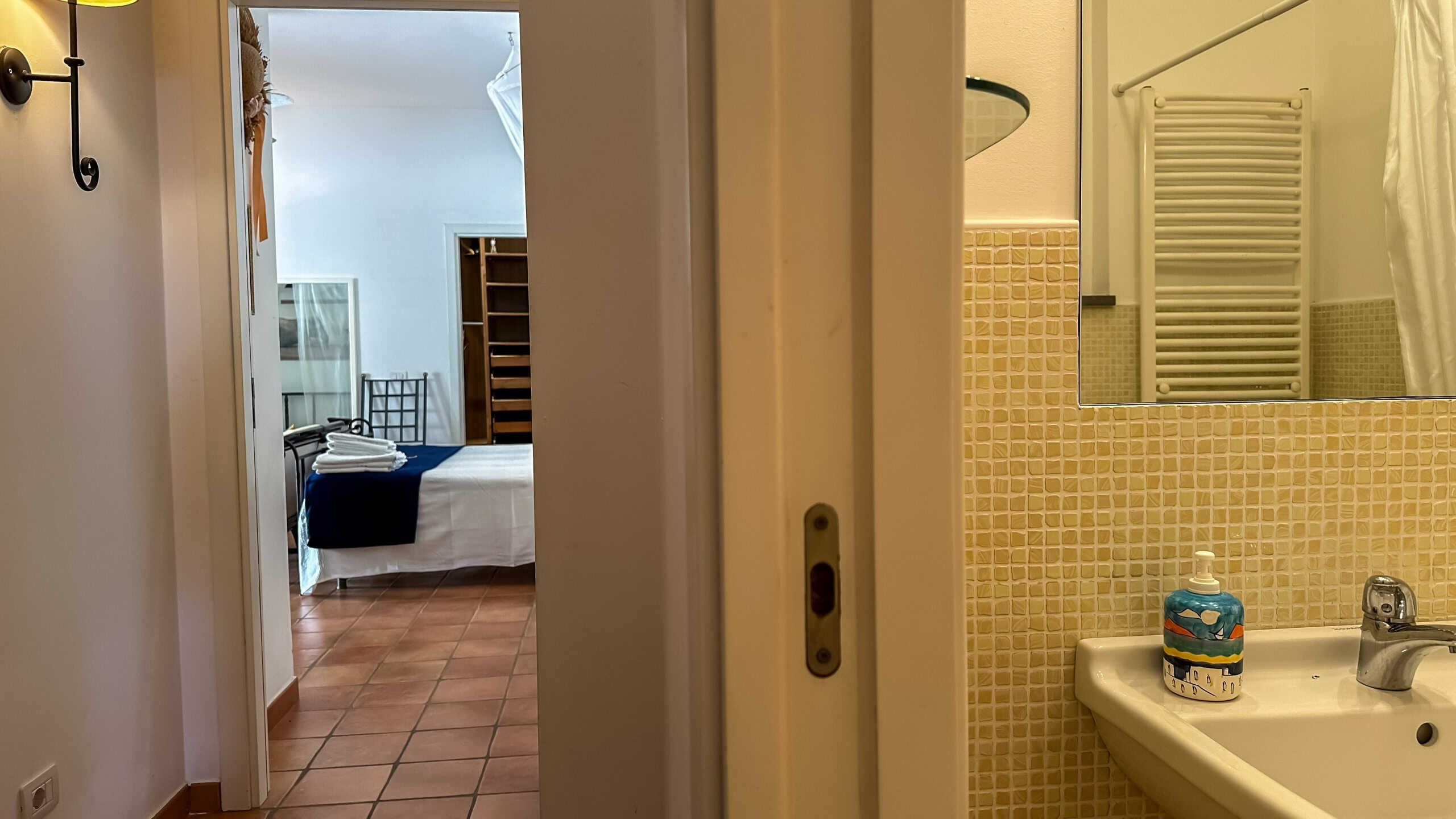 Spazio bagno e camera da letto in appartamento turistico NextCasa, arredamento accogliente con dettagli funzionali, pavimentazione in piastrelle, ambiente luminoso e confortevole, ideale per soggiorni in città.