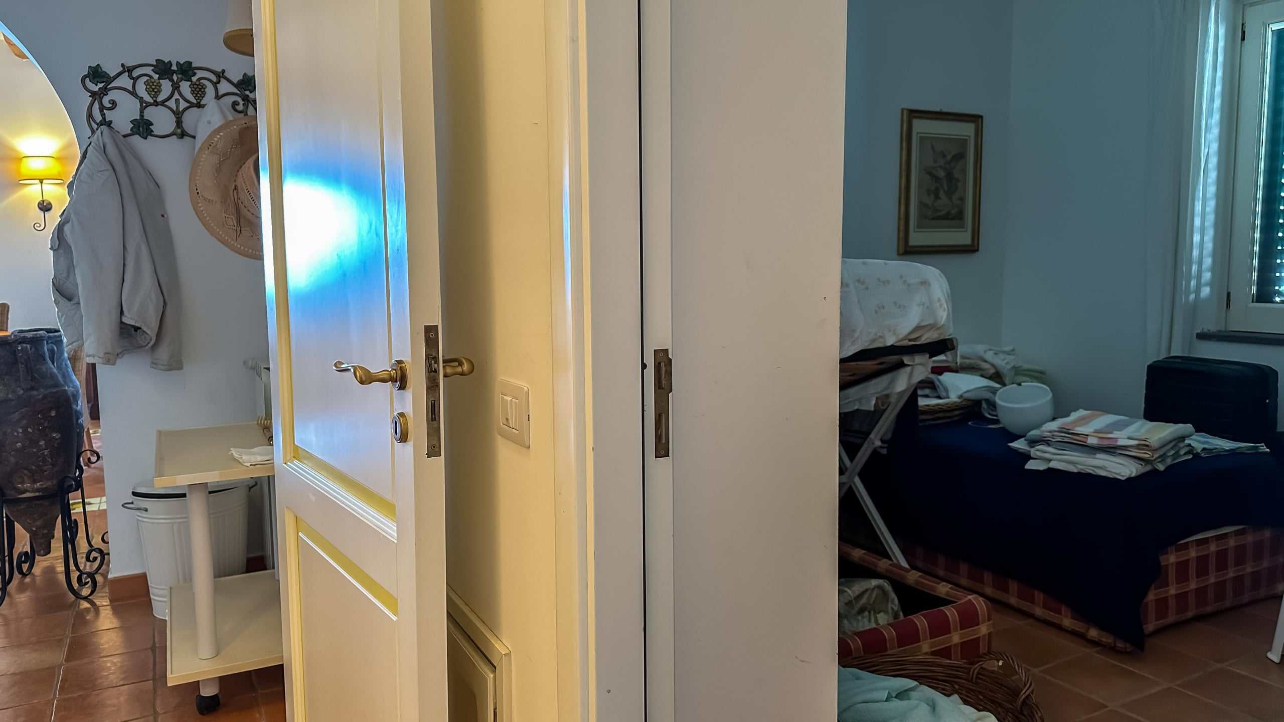 Porta di ingresso con vista sulla camera da letto e oggetti casalinghi, interni di un appartamento arredato con stile semplice e funzionale, atmosfera domestica calda e accogliente, ambiente con illuminazione naturale.