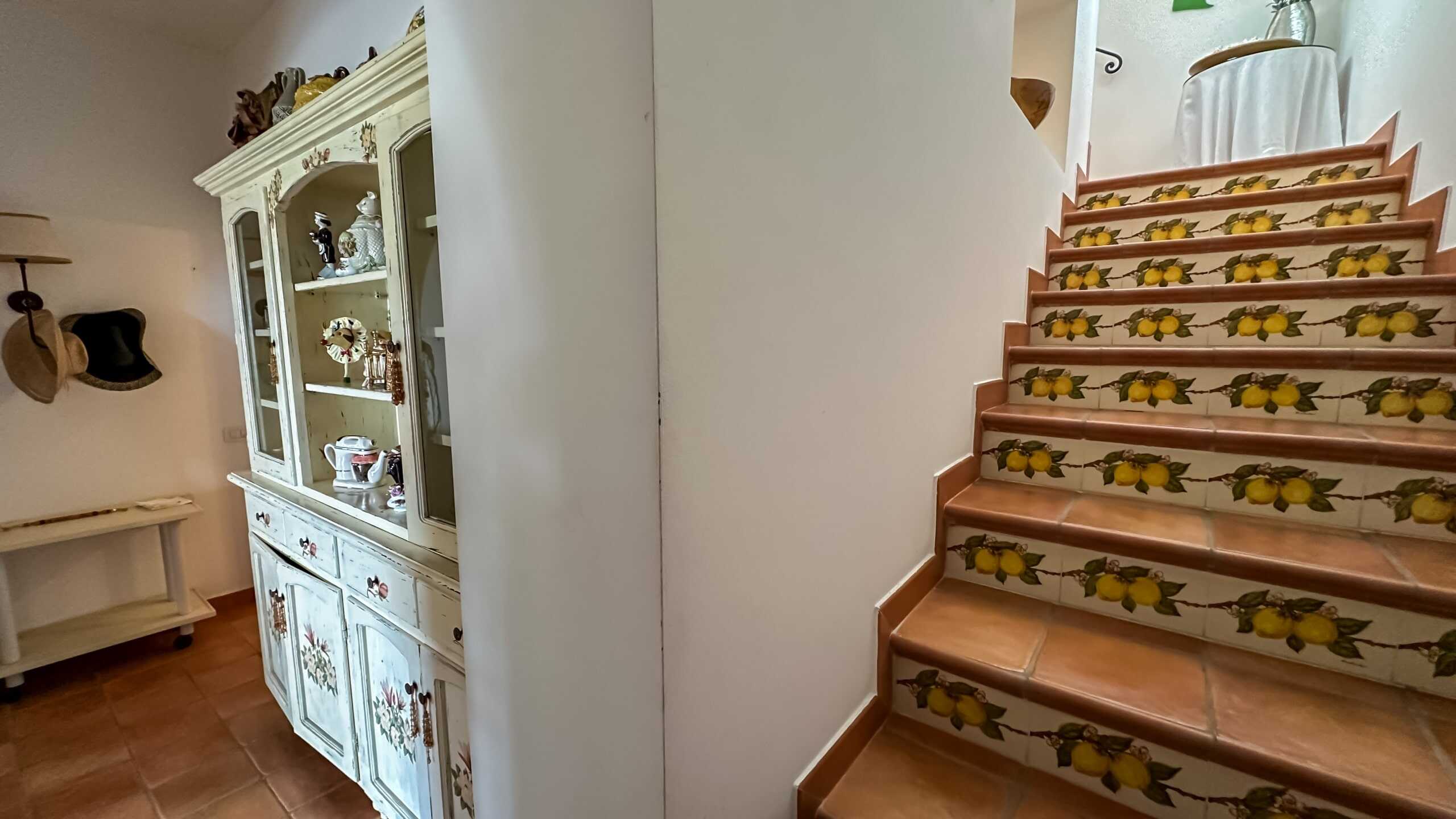 Fondo di una scala con piastrelle decorate con limoni gialli, spazio interno di una casa in stile classico, arredamento tradizionale e dettagli artistici, ambiente accogliente e luminoso.