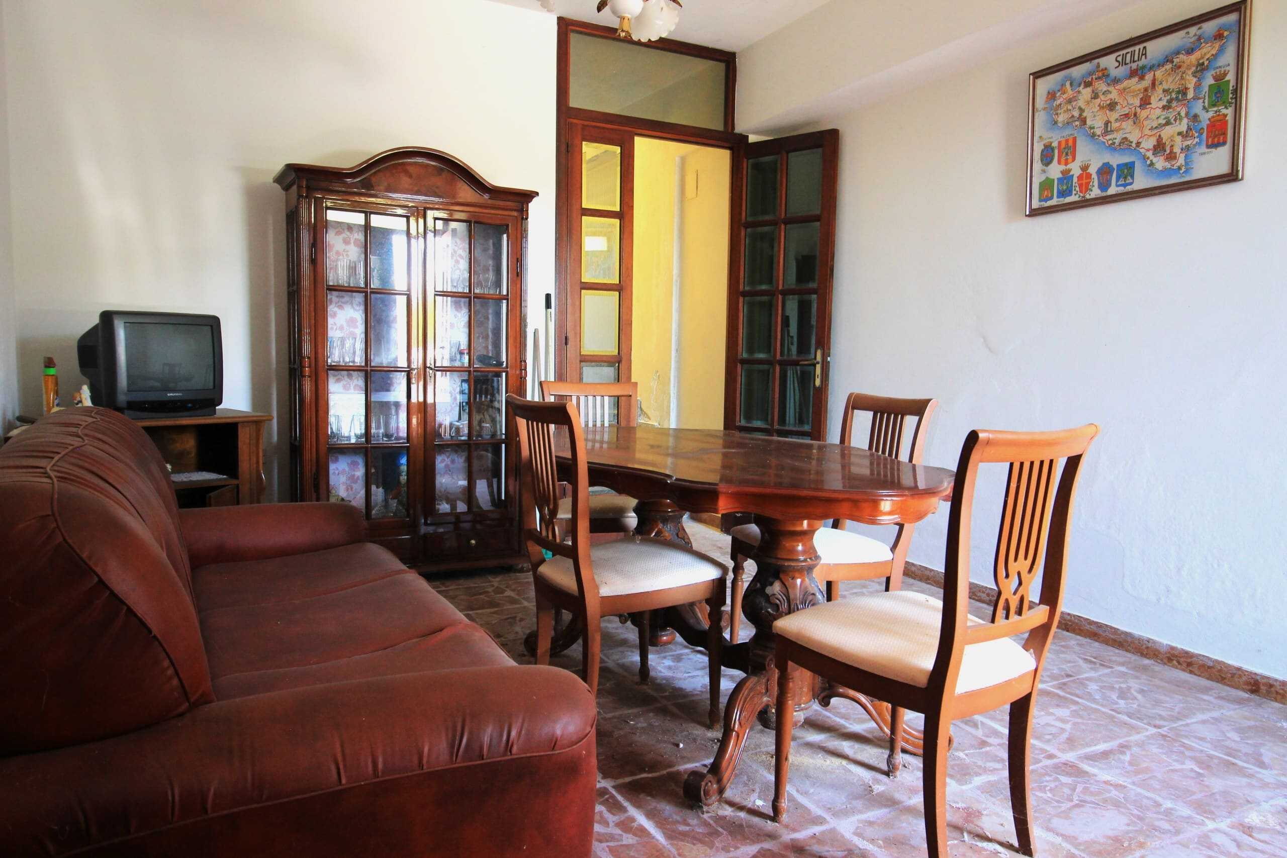 Soggiorno con mobili in legno, divano in pelle rossa e tavolo da pranzo in stile classico in una casa privata, decorata con mappa della Sicilia e arredi tradizionali.