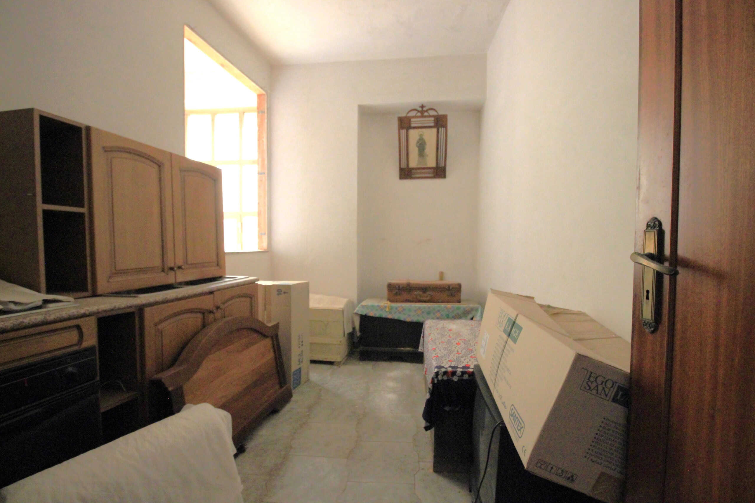 Stanza di casa con mobili in legno, finestra luminosa, scatole e arredi vari, ambienti da ristrutturare, spazio abitativo rustico, mobilio e dettagli di arredamento in stile tradizionale, NextCasa immobiliare.