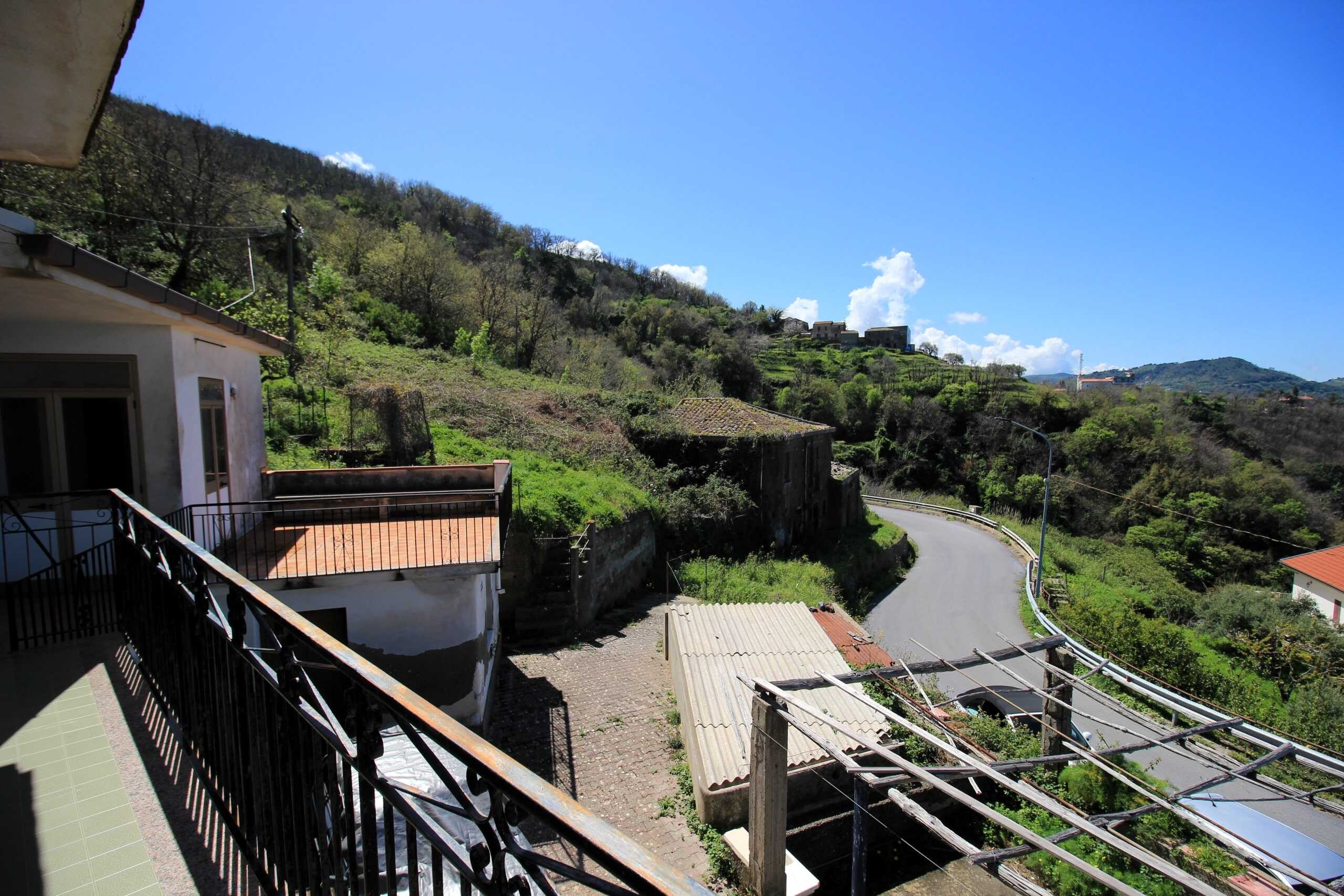 Ampli vista sulla collina con case e strade serene, paesaggio naturale verdeggiante, tradizionale architettura di montagna, cielo azzurro e luce naturale, perfetta per un'immagine di immobili o case in collina.