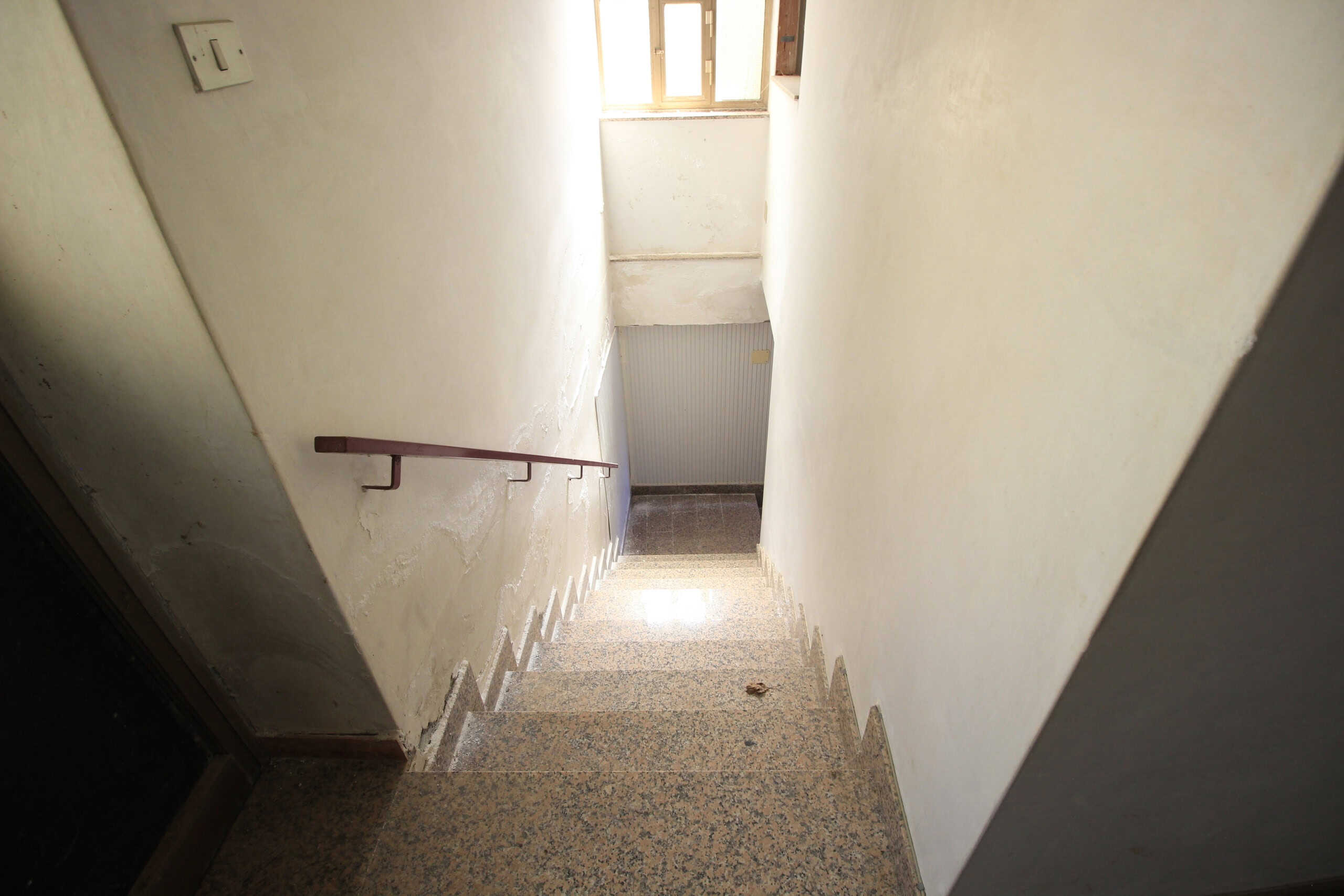 Scala interna di un appartamento in fase di ristrutturazione, con pareti bianche e ringhiera in legno, che conduce al piano superiore o al piano terra.