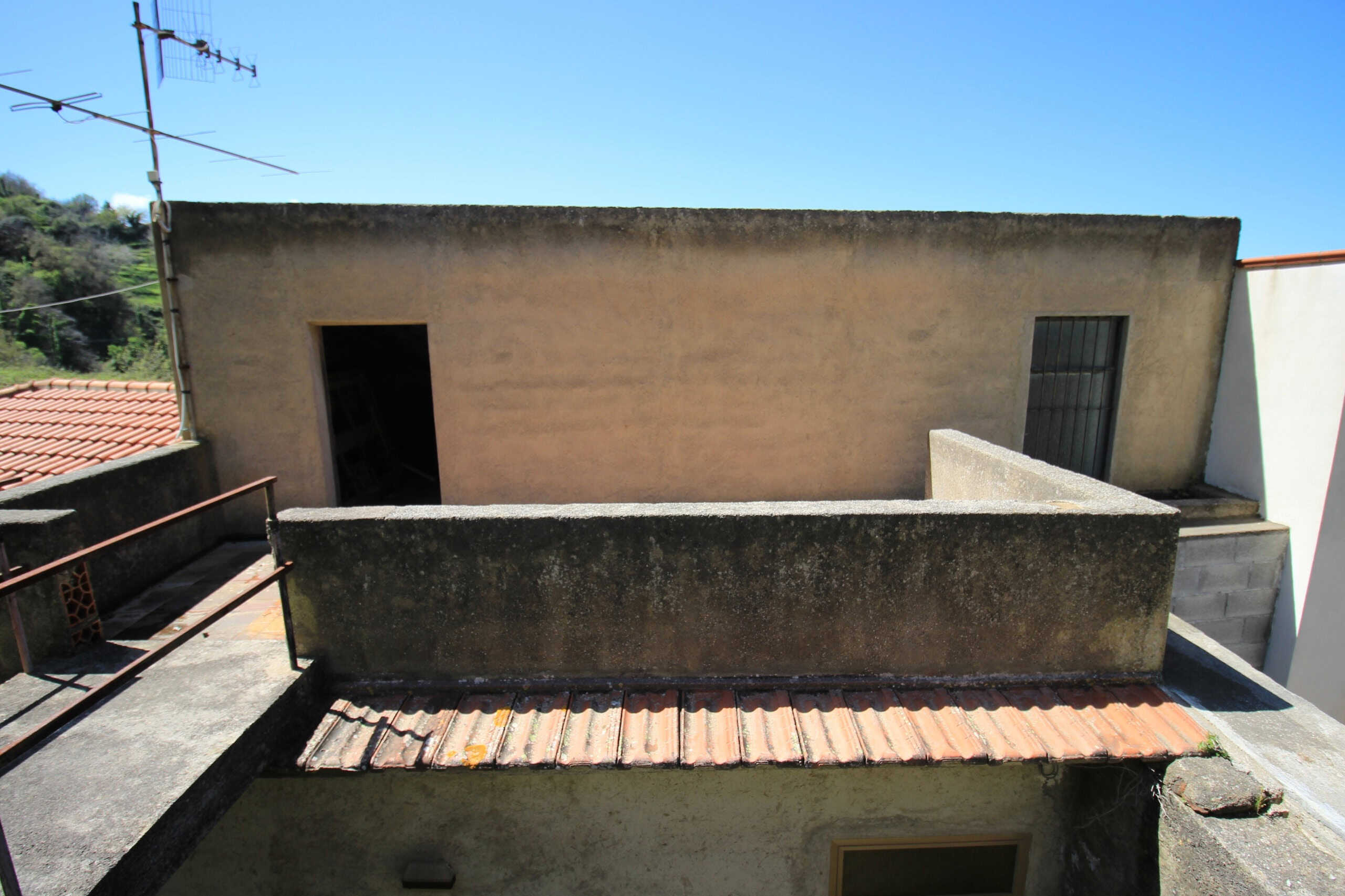Balcone di appartamento in fase di ristrutturazione, vista in alto con pareti di cemento e terrazza in piastrelle di terracotta.