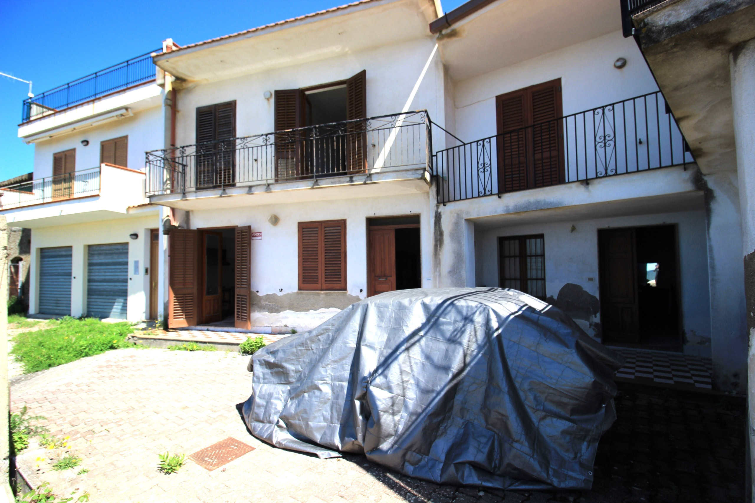 Auto in cortile davanti a una casa bifamiliare con balconi e persiane in legno, in condizioni di ristrutturazione, con murature in via di rinnovo a Venezia, Italia.
