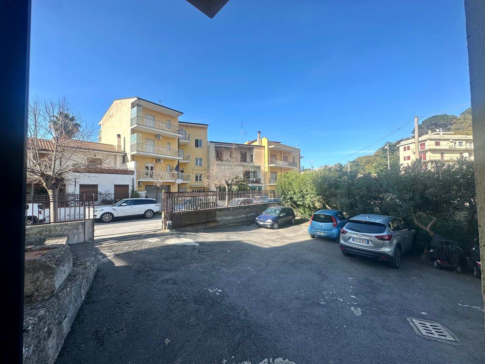 Parcheggio condominiale all'aperto con auto parcheggiate, vista su edifici residenziali e un cielo sereno, ideale per trovare facilmente un posto macchina in zona.