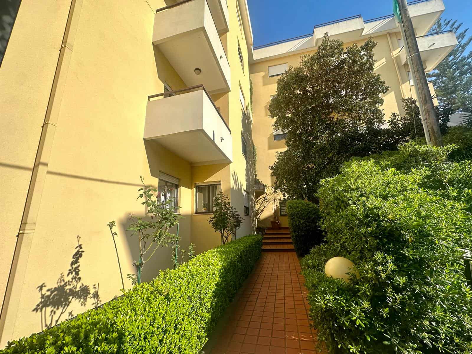 Villa moderna con giardino curato e piante rigogliose, ingresso con scalini in mattonelle rosse, ambienti luminosi e balconi spaziosi, ideale per vivere all'aperto e in confort a pochi passi dalla città.