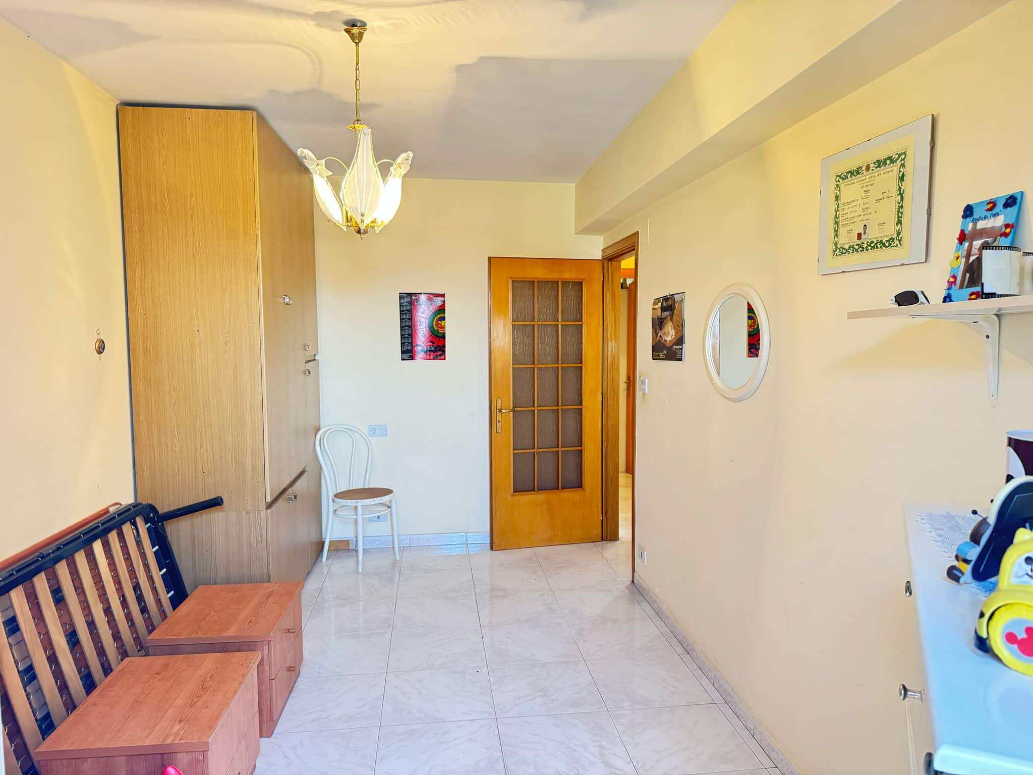 Soggiorno luminoso con pareti gialle, armadio in legno, sedie bianche, porta a vetri e dettagli decorativi, ideale per ambienti residenziali o immobili in vendita e affitto.