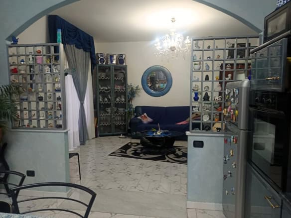 1. Divano blu in soggiorno con arredamento elegante e scaffalature con oggetti decorativi, illuminata da lampadario centrale.