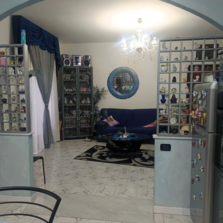 1. Divano blu in soggiorno con arredamento elegante e scaffalature con oggetti decorativi, illuminata da lampadario centrale.