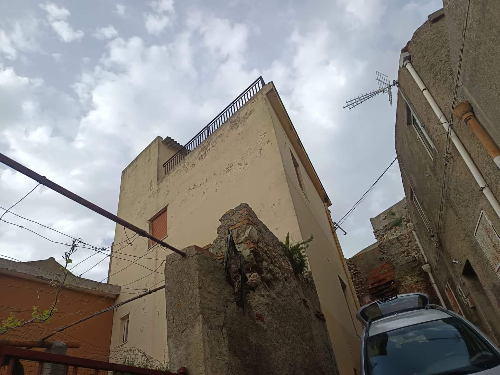 Tetto di edifici residenziali in stile mediterraneo in zona urbana, con oblò e antenne TV, cielo nuvoloso, inquadratura dall'esterno con veicoli parcheggiati, rappresenta la vita quotidiana e l'architettura locale.