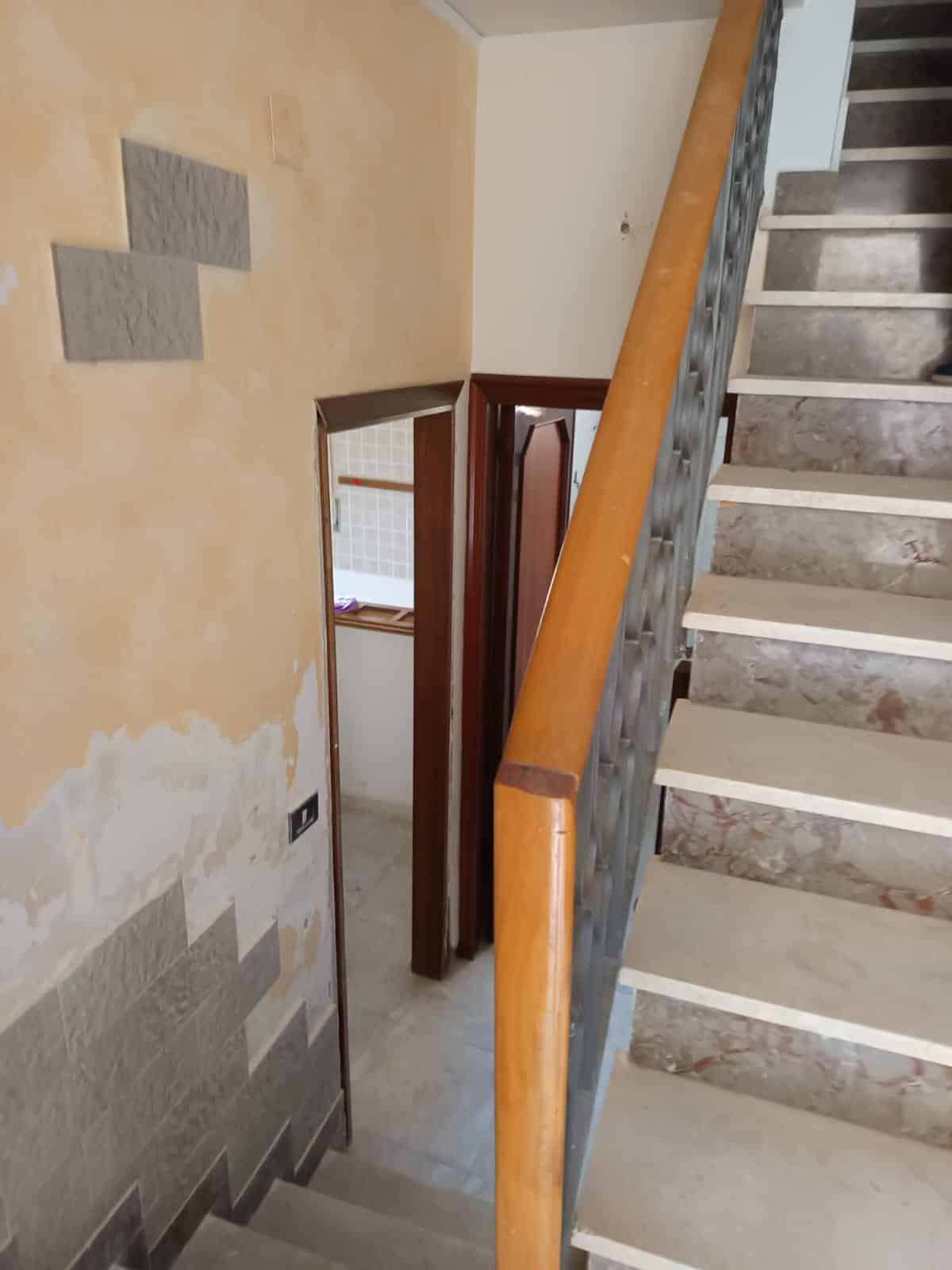 Filo immagine, Alt testo, Leggero sguardo a una scala interna in fase di ristrutturazione, con pareti in decorazione da rinnovare, toni neutri e elementi in legno, ambiente di casa in preparazione.