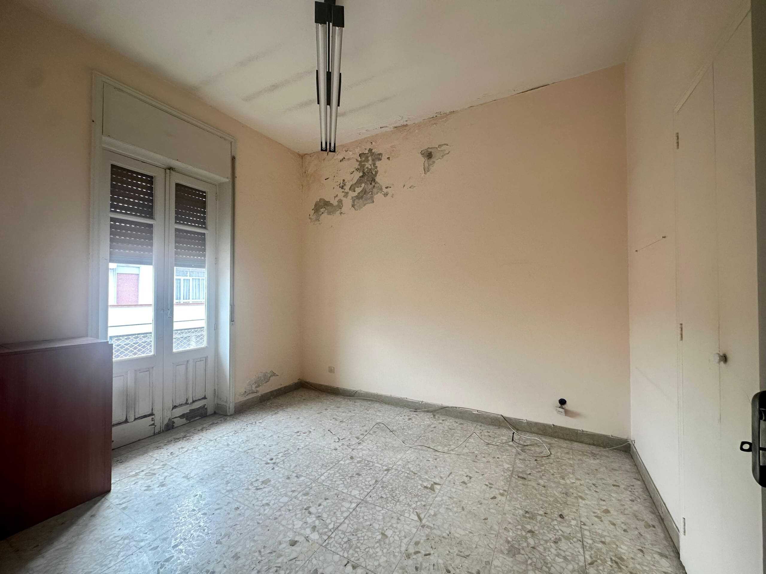 Finestra con persiane e pareti in fase di ristrutturazione, camera vuota con pavimento in marmo, presenza di lavori di manutenzione, esposizione alla luce naturale, ambiente spazioso e luminoso.